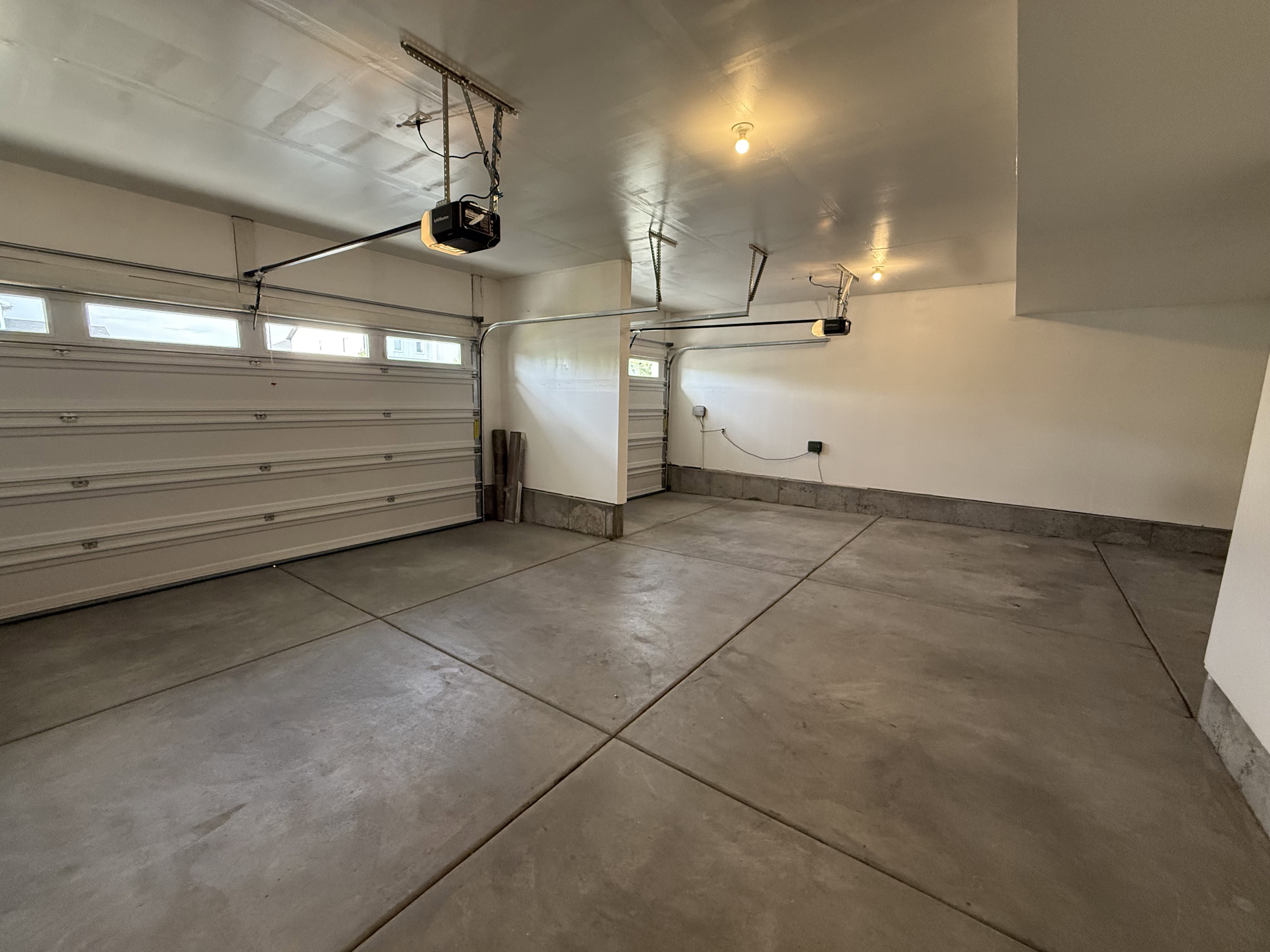 Spacious garage featuring a concrete floor, painted walls, overhead lighting, and two garage door openers