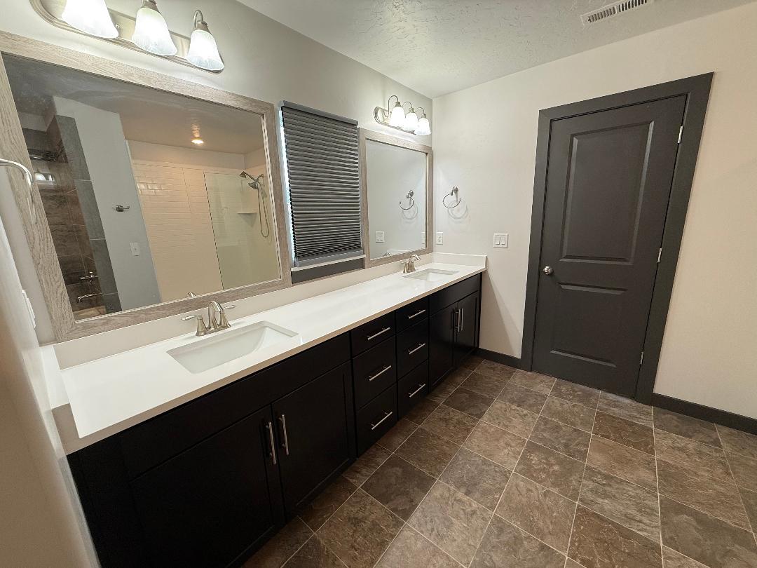 Spacious bathroom featuring a dual vanity with white countertops, dark cabinetry, and two framed mirrors in master bath