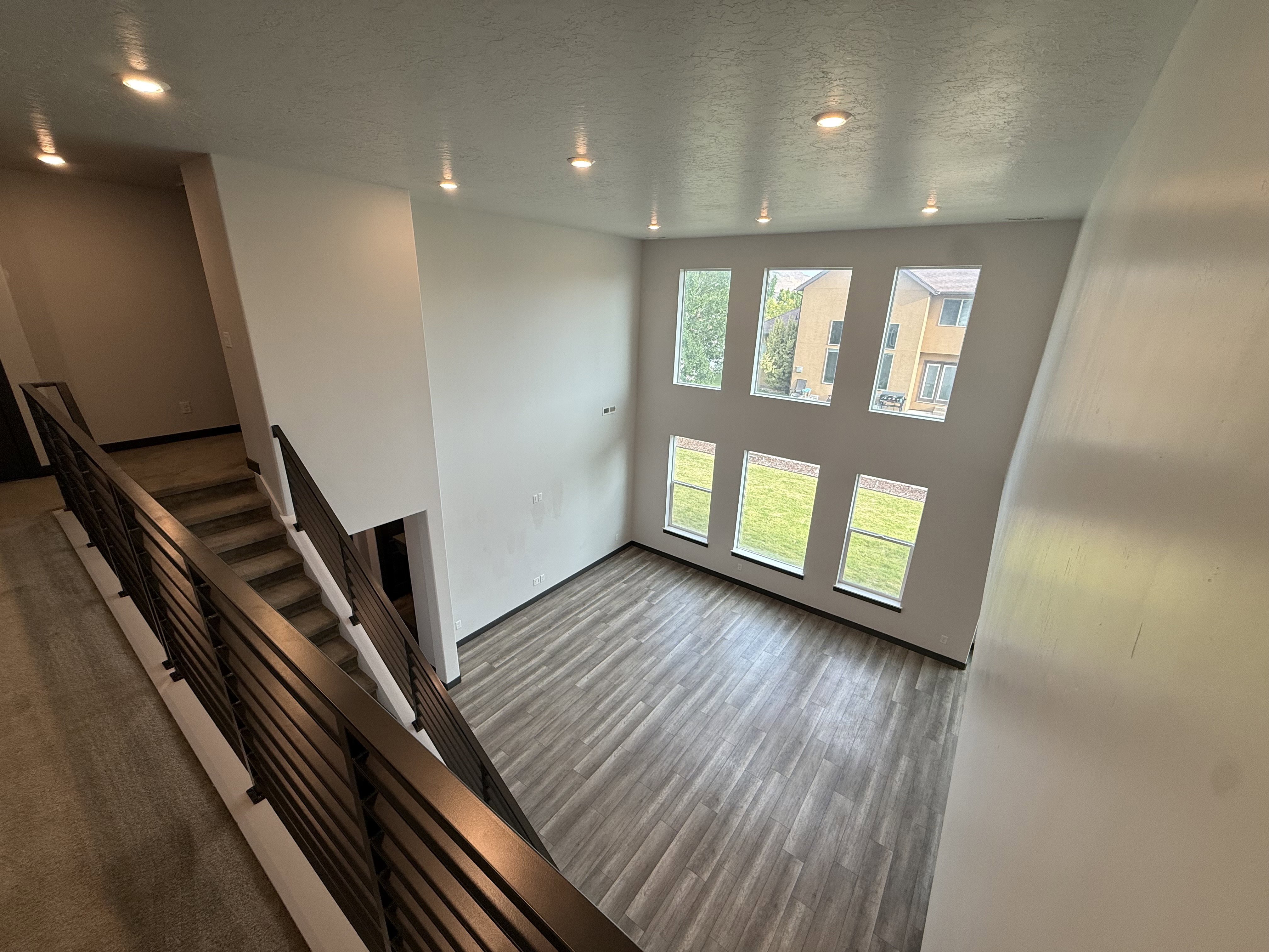 Two-story living area featuring a wall of six rectangular windows, recessed lighting, and wood-finish flooring