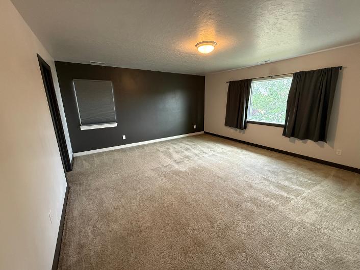 Spacious master bedroom featuring neutral carpet flooring and a contrasting accent wall
