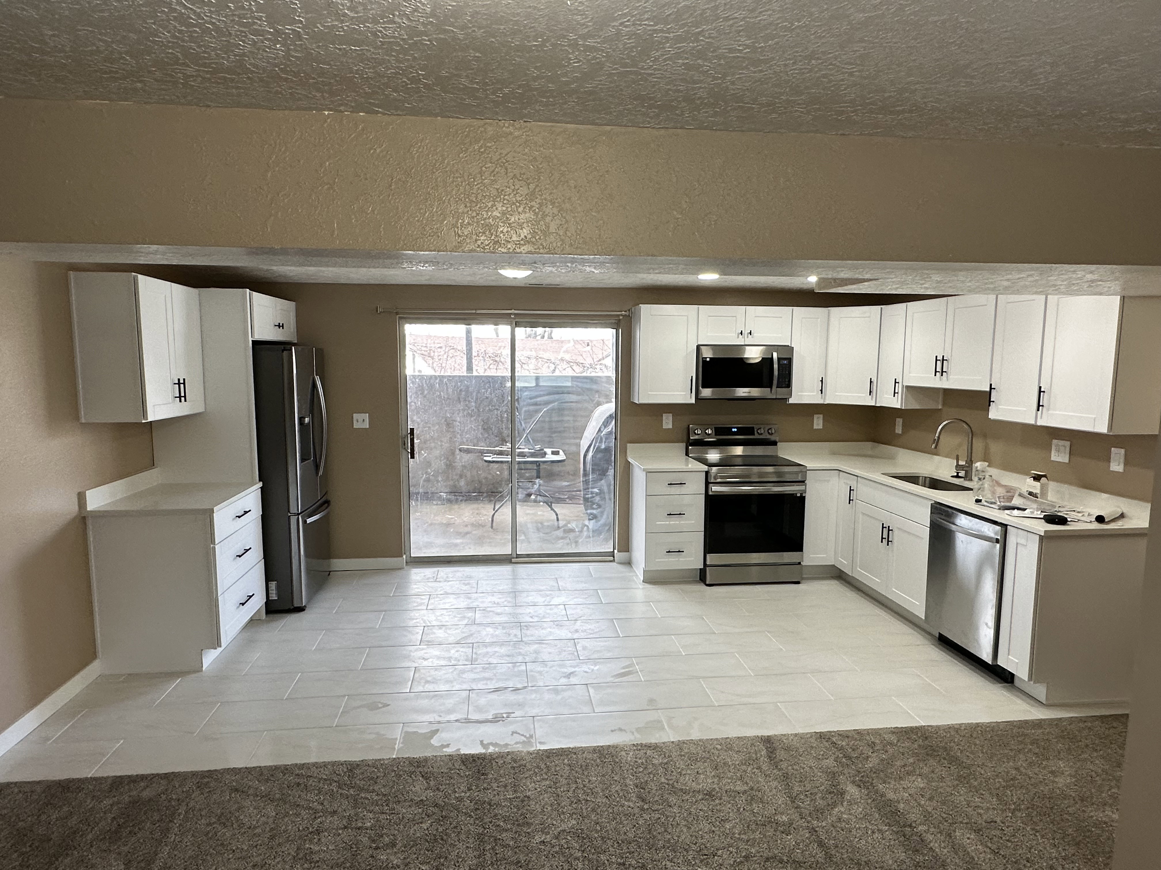 Modern kitchen featuring white shaker cabinetry, stainless steel appliances, light-toned countertops, and light-colored tile flooring