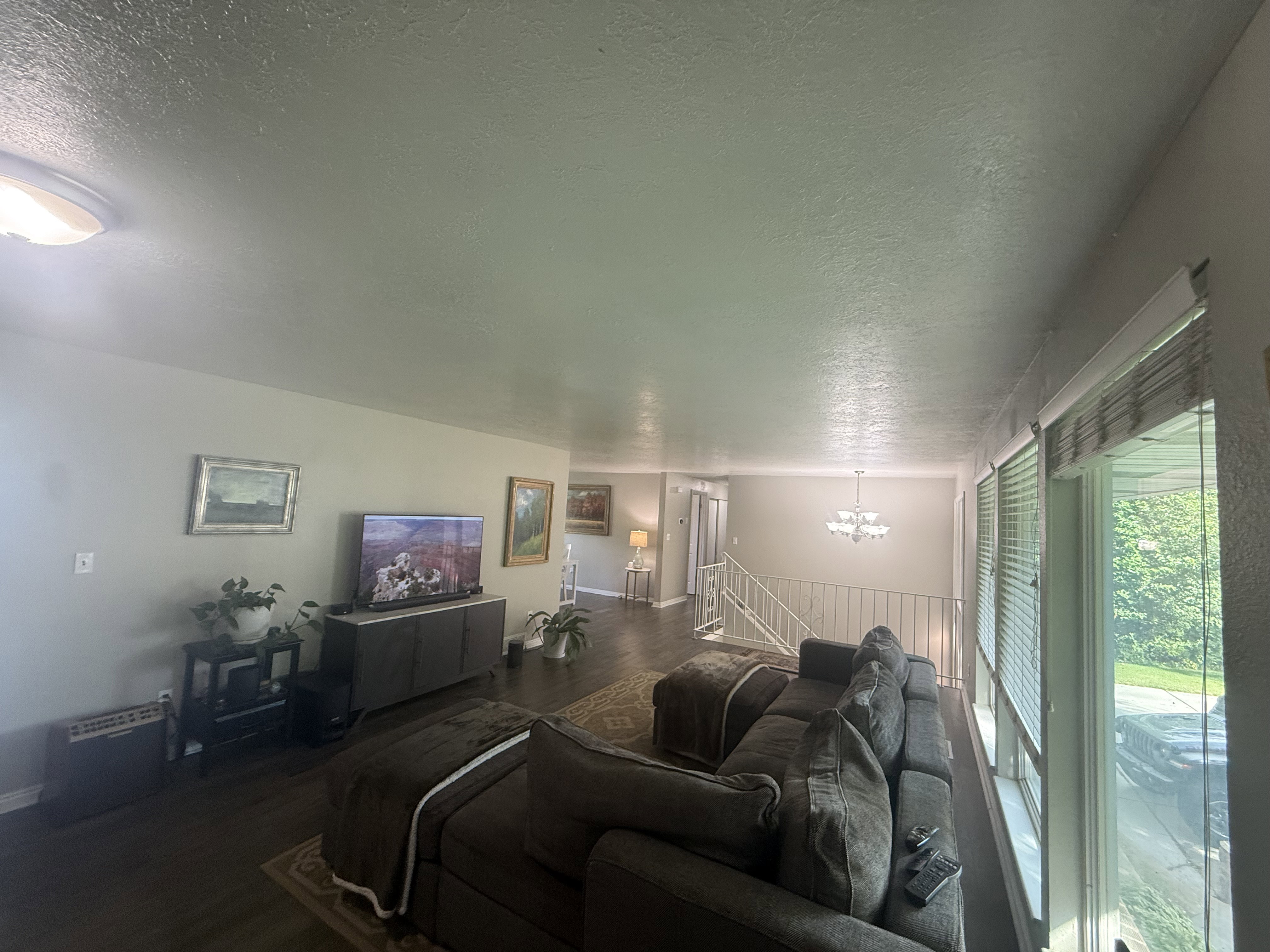 Spacious living area featuring wood-finish flooring, ample natural light from large windows, and a dedicated dining space with a chandelier