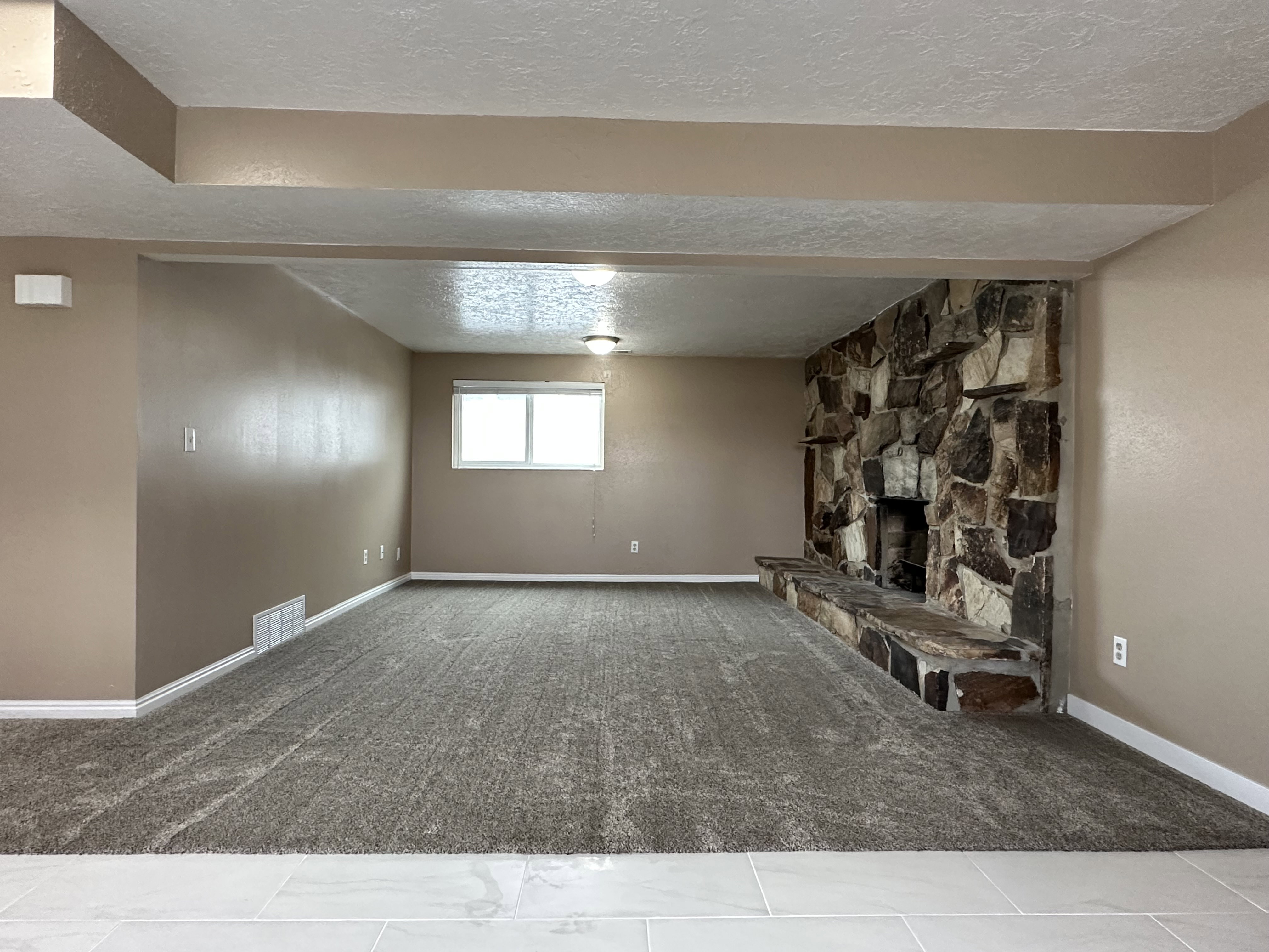 Spacious room featuring a stone fireplace with hearth, plush carpet flooring, a large window, and recessed lighting