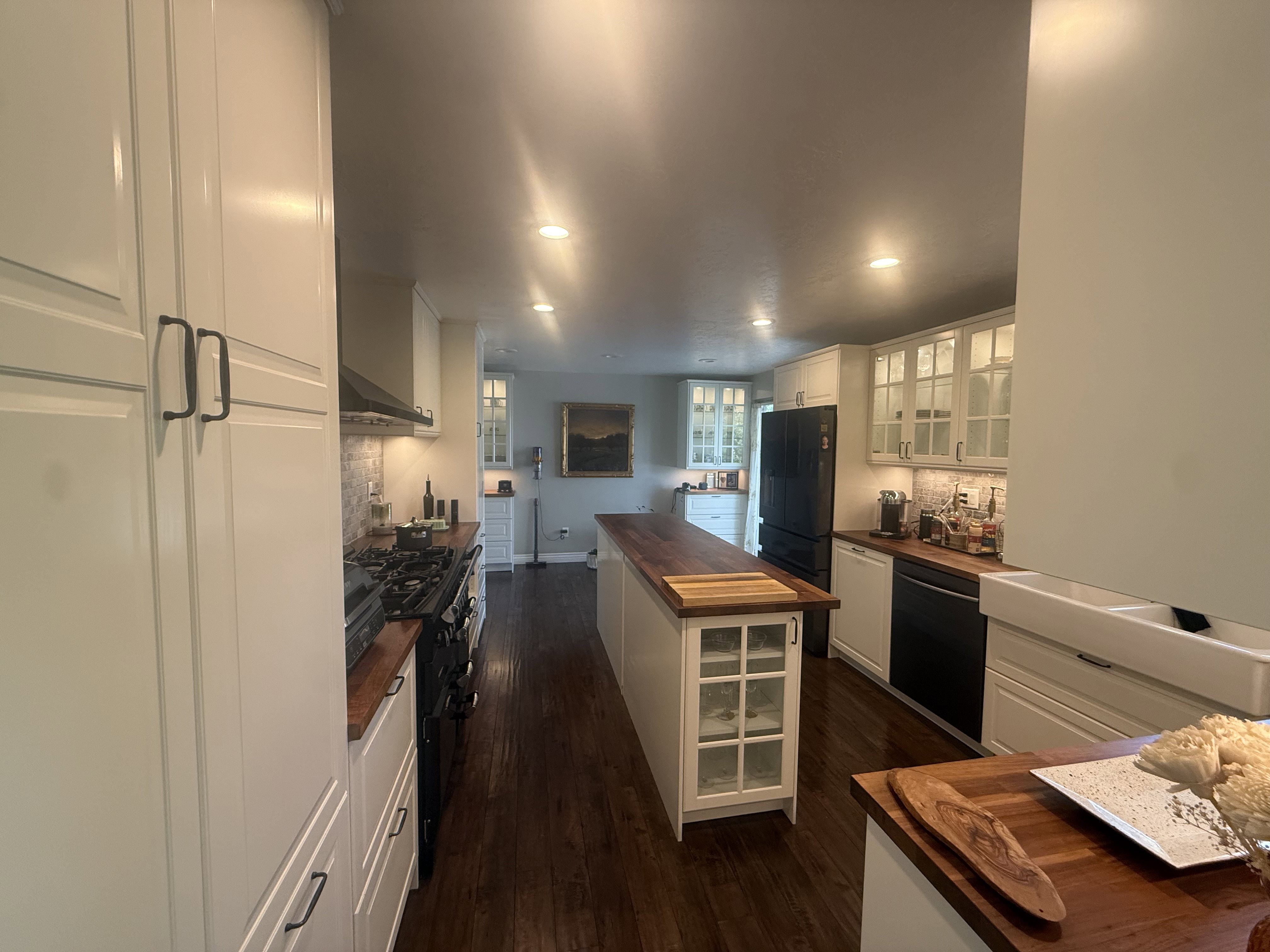 Bright kitchen featuring white shaker cabinetry, dark wood-finish flooring, butcher block countertops, a center island with built-in storage, and integrated appliances