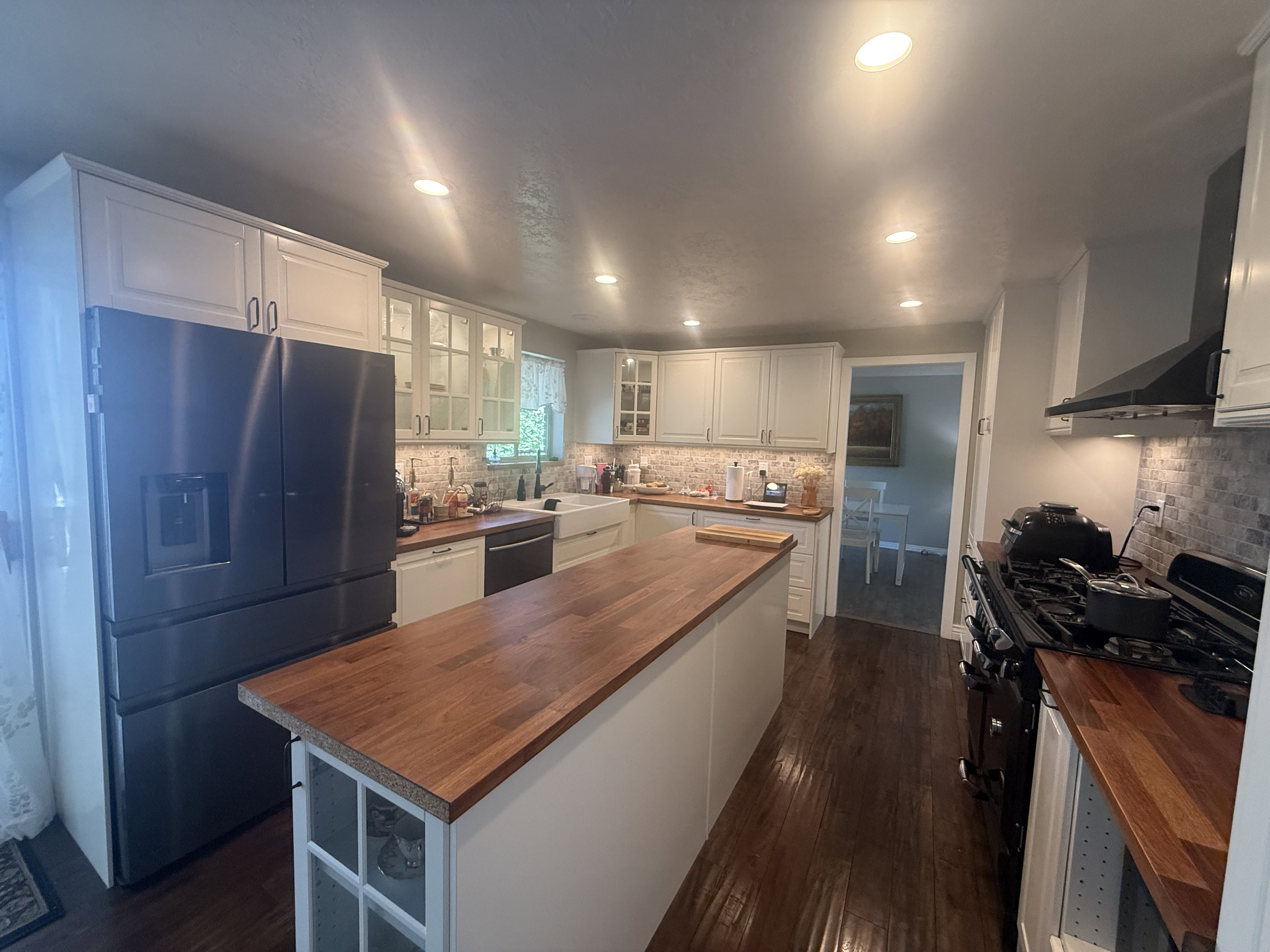 Spacious kitchen featuring an island with a wood-finish countertop, stainless steel refrigerator, white cabinetry, dark wood-finish flooring, and recessed lighting