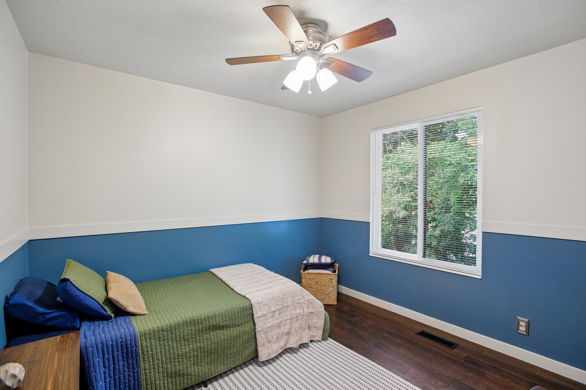 Bedroom featuring wood-finish flooring, a white-framed window with blinds, and a ceiling fan with integrated lighting