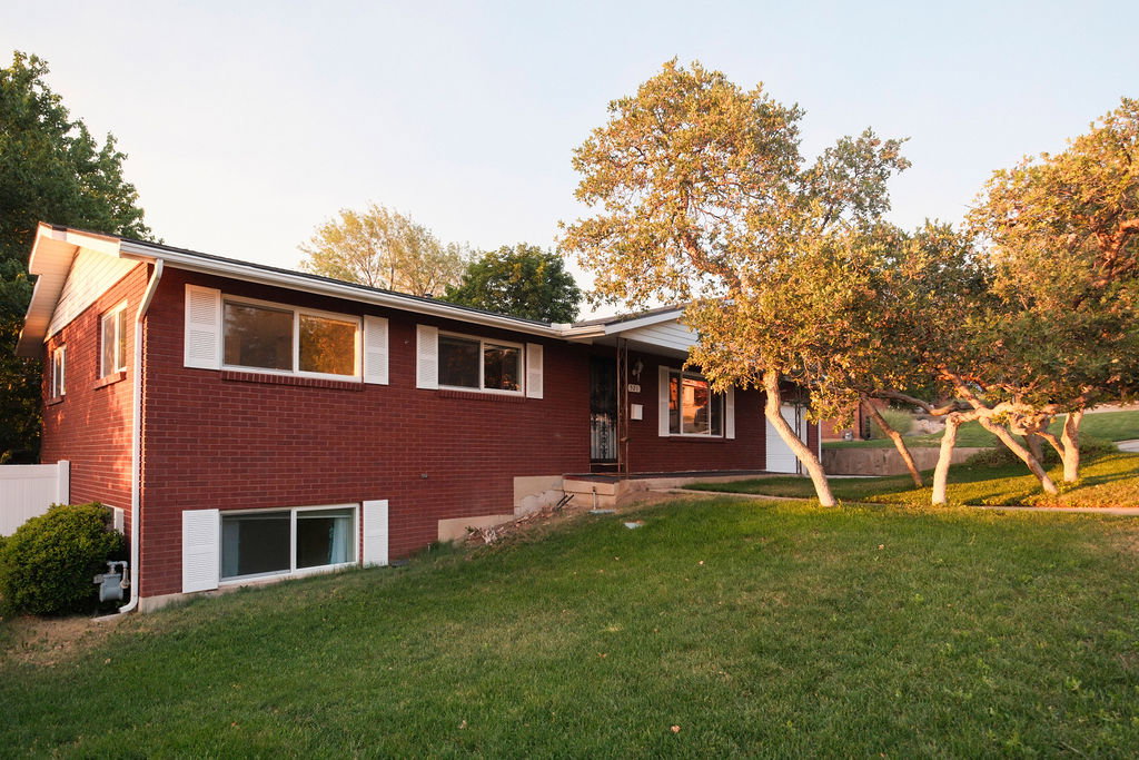 Red brick exterior with white decorative shutters, a covered entry, and mature trees