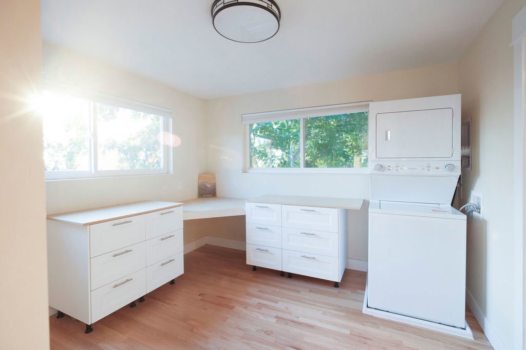 Spacious room featuring wood-finish flooring, multiple windows, a built-in corner desk, and white cabinetry with wood-look countertops