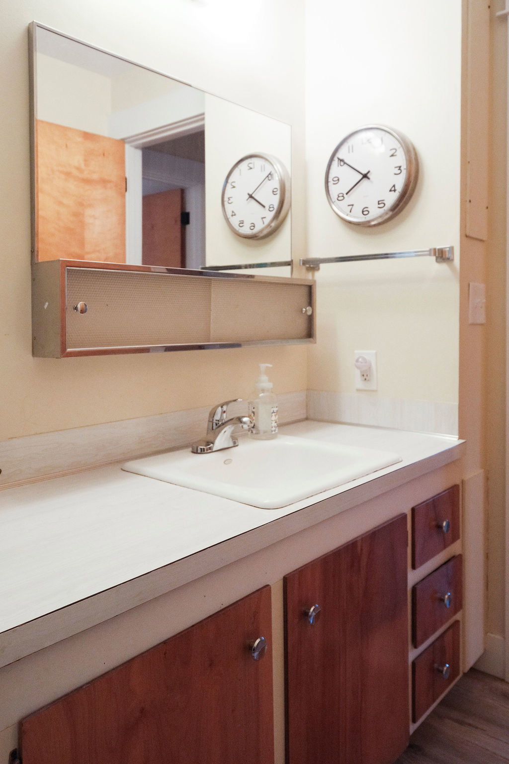 Bathroom vanity featuring a white countertop with an integrated sink, chrome faucet, and wood-finish cabinetry