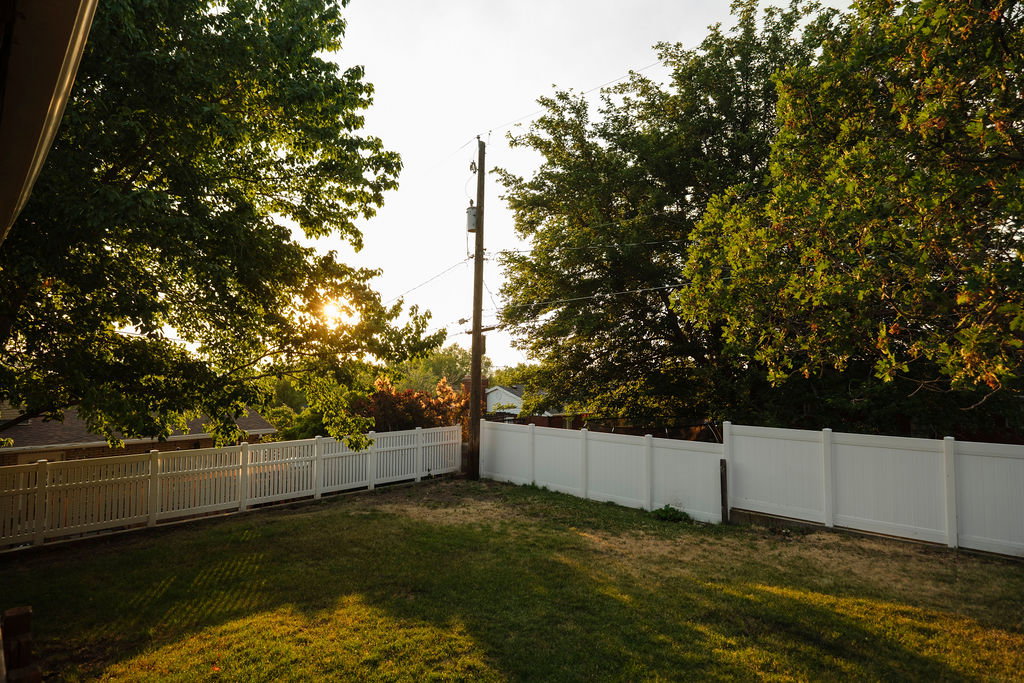 Expansive backyard featuring a manicured lawn, a white picket fence, a solid white privacy fence, and mature trees
