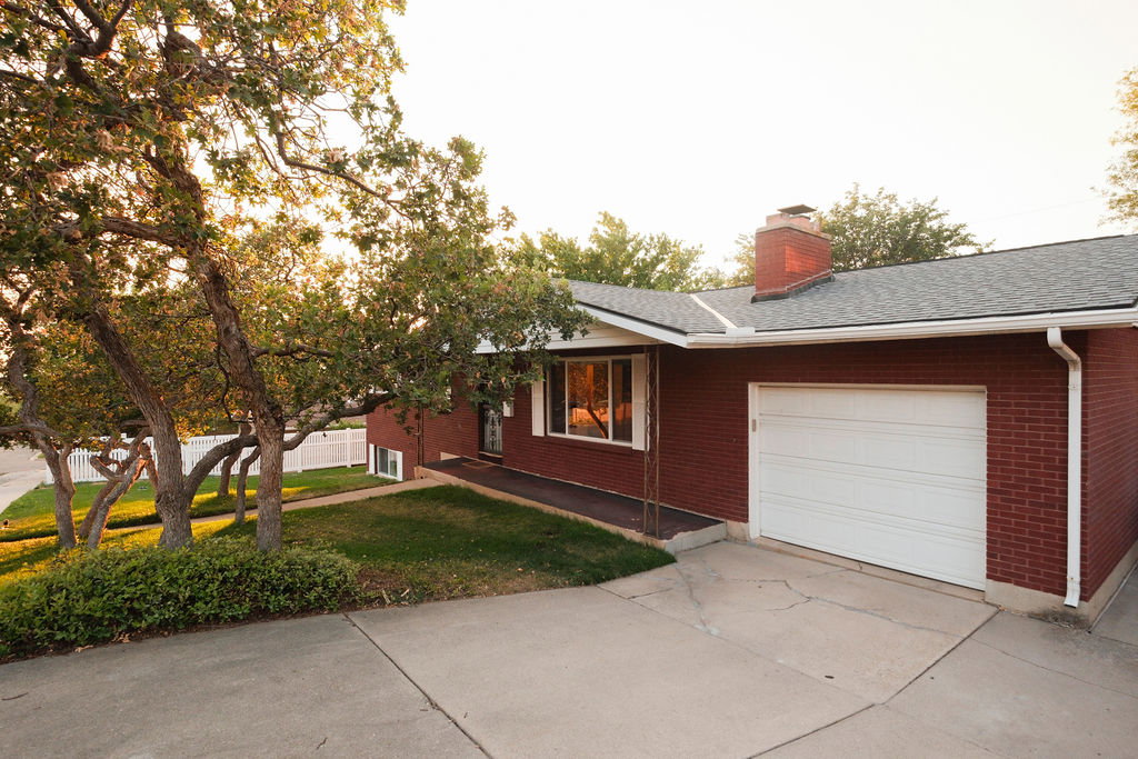 Red brick exterior featuring a white garage door, asphalt shingle roof, and a red brick chimney