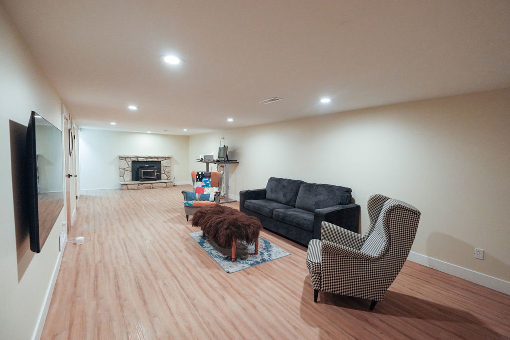 Spacious room featuring wood-finish flooring, recessed lighting, and a stone-clad fireplace with a wood-burning insert