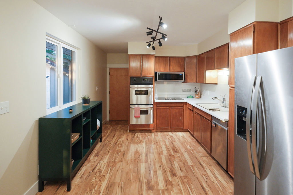 Kitchen featuring wood-finish flooring, warm wood cabinetry, stainless steel appliances, and a modern track light fixture