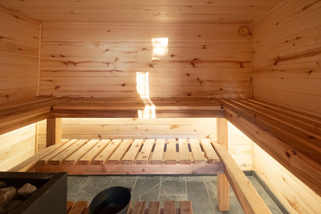 Sauna room featuring natural wood paneling, multi-level slatted wooden benches, and dark stone tile flooring