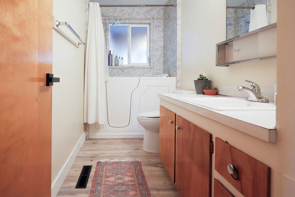 Bathroom featuring a walk-in tub with a shower, a vanity with wood-finish cabinetry, a built-in sink, and wood-finish flooring