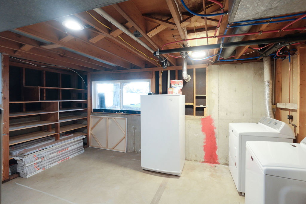 Lower level utility area featuring exposed wood joists, concrete flooring, built-in shelving, a window, and laundry appliances
