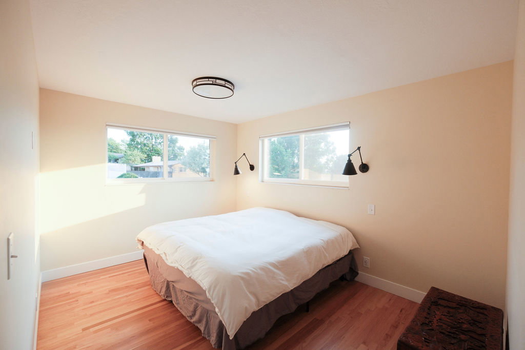 Bedroom featuring wood-finish flooring, dual windows, two wall-mounted sconces, a ceiling-mounted light fixture, and light-toned wall paint
