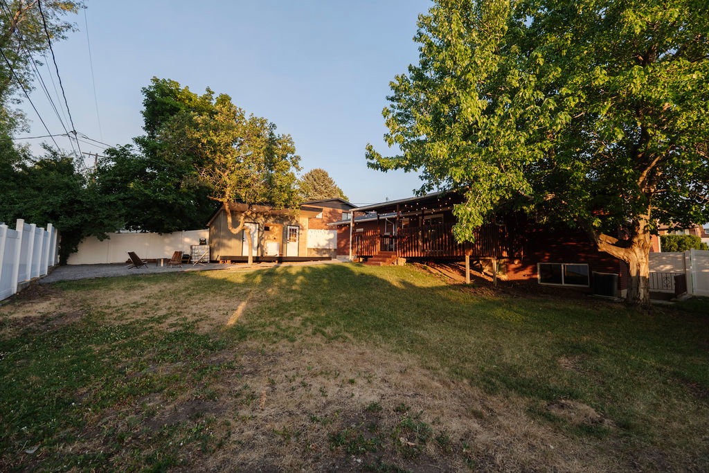 Expansive backyard featuring a large green space, mature trees, and a privacy fence
