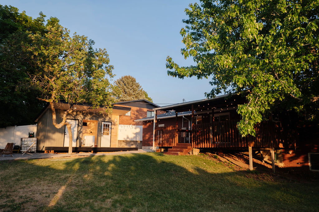 Expansive backyard featuring a lush lawn, mature trees, and a spacious wood-finish deck with a covered area