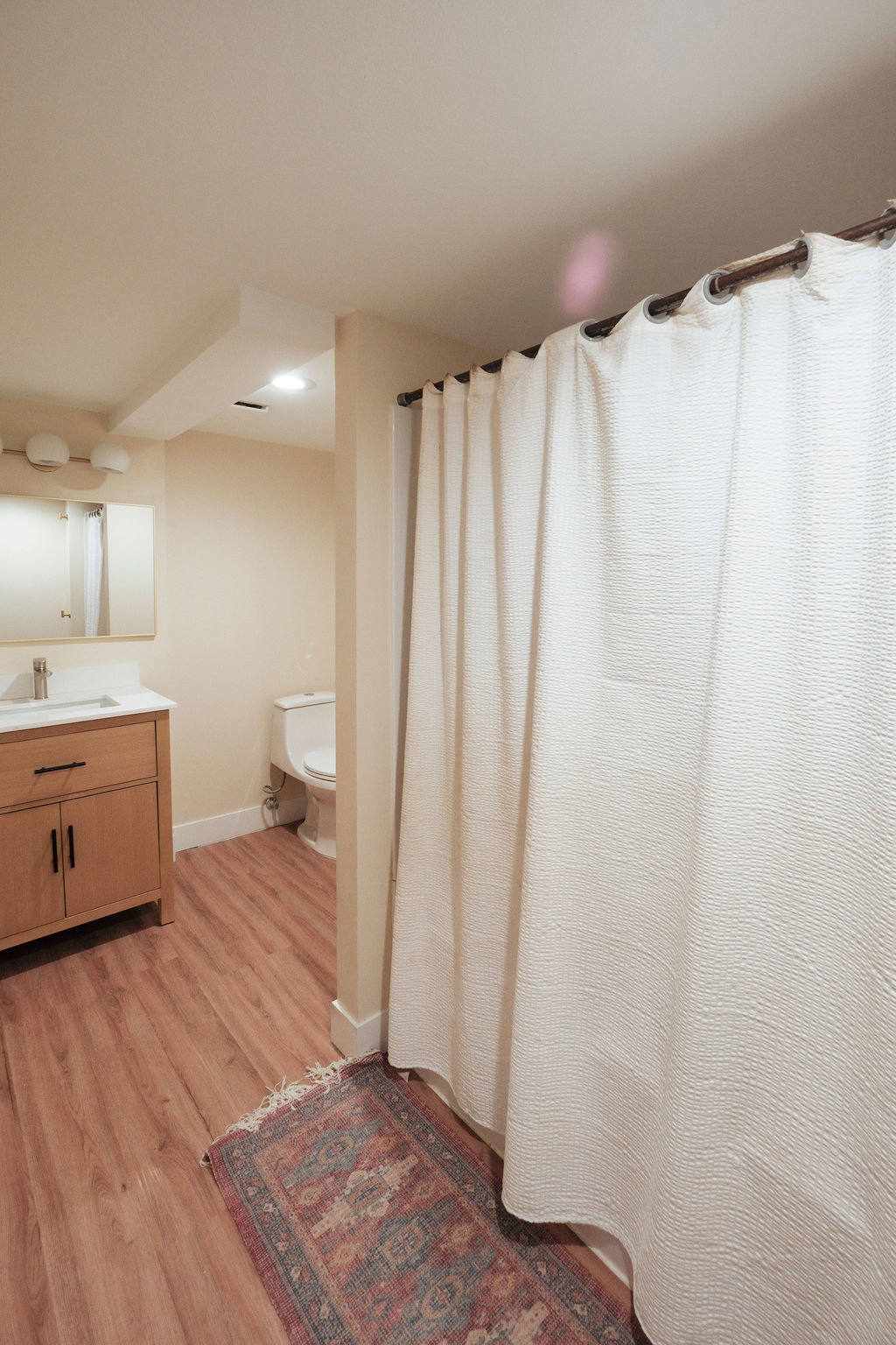 Bathroom featuring wood-finish flooring, a vanity with under-sink storage, a wall-mounted mirror, and a white toilet