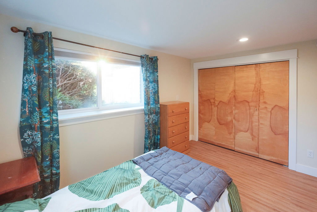 Bedroom featuring wood-finish flooring, a window with exterior landscaping, a recessed ceiling light, and bi-fold closet doors with white trim