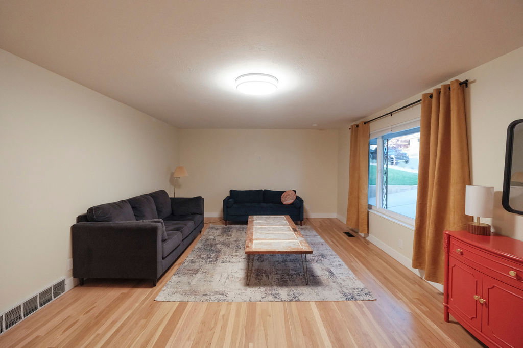 Spacious living area featuring light wood-finish flooring, neutral wall tones, and a large window providing natural light