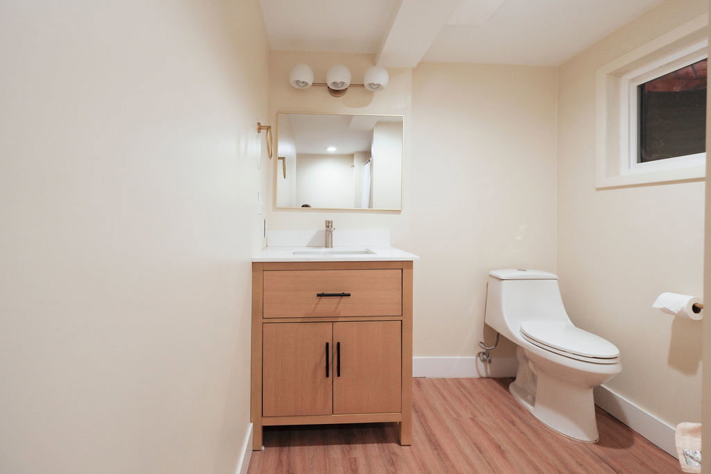 Bathroom featuring a light wood-finish vanity with a white countertop and rectangular sink, a wall-mounted mirror, and a modern toilet