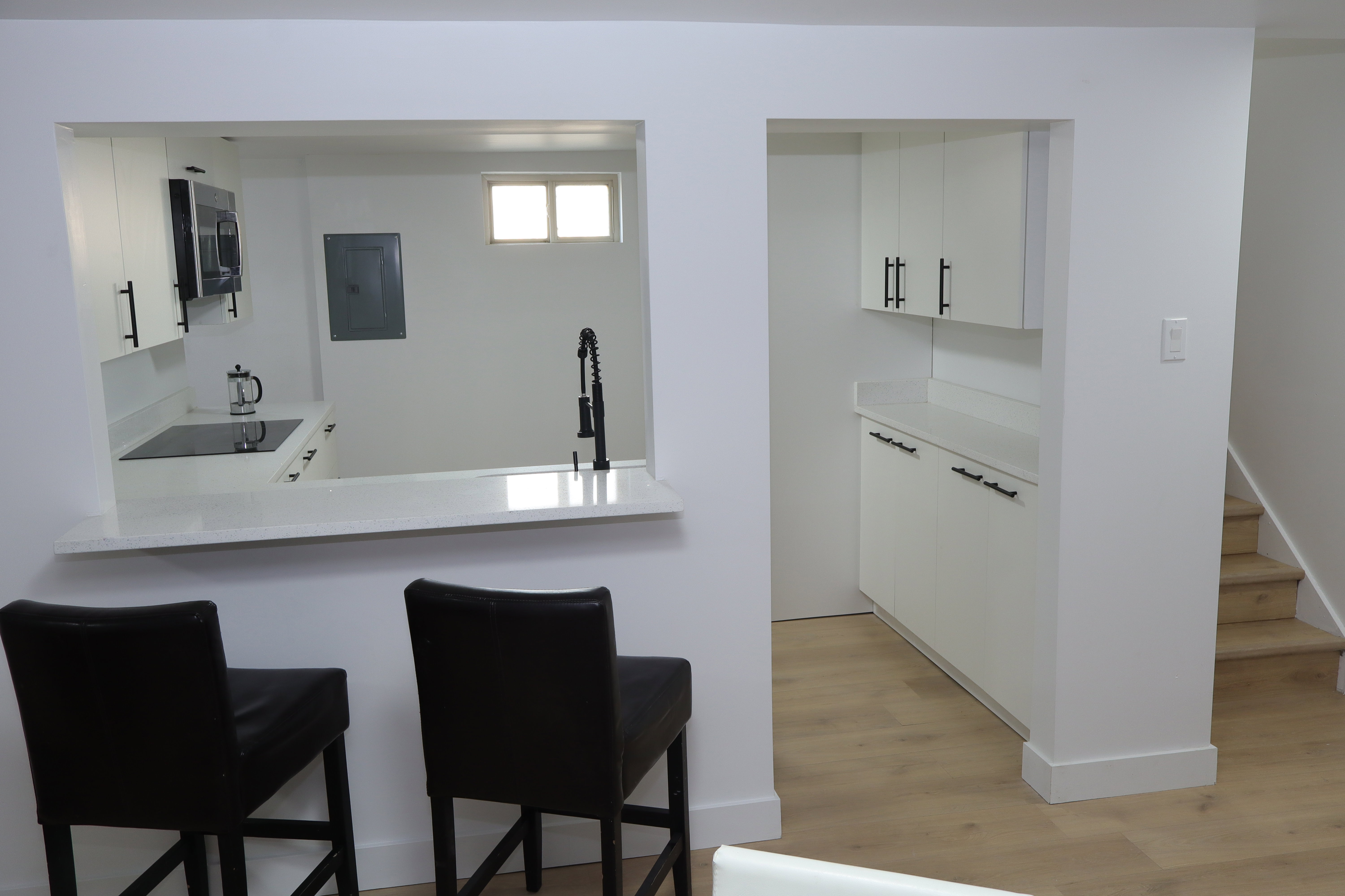 Kitchenette featuring a pass-through counter, white cabinetry with dark hardware, a built-in cooktop, and a wall-mounted microwave