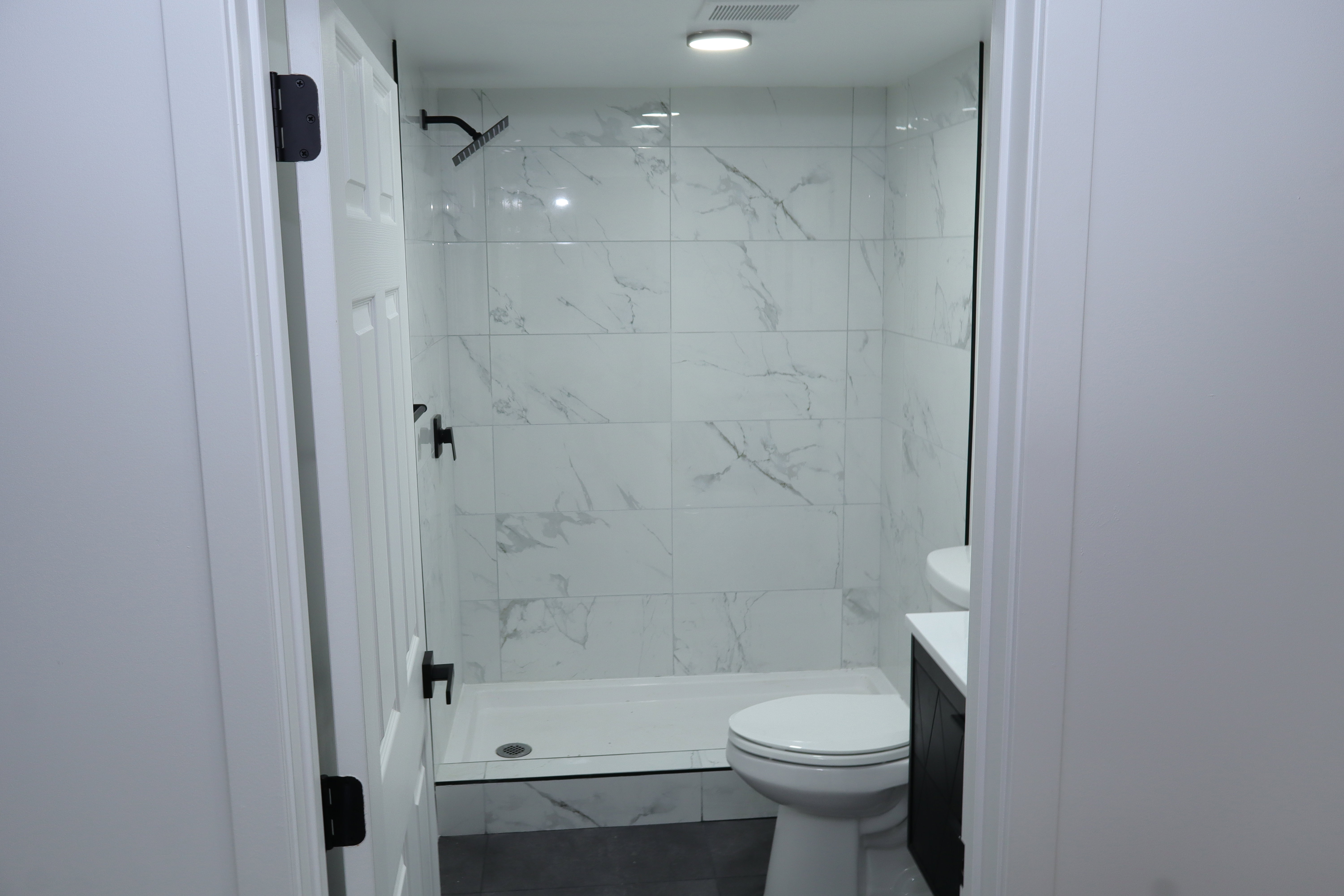 Modern bathroom featuring a tiled shower with matte black fixtures, a white shower pan, a wall-mounted toilet, and a dark wood-finish vanity with a white countertop and vessel sink