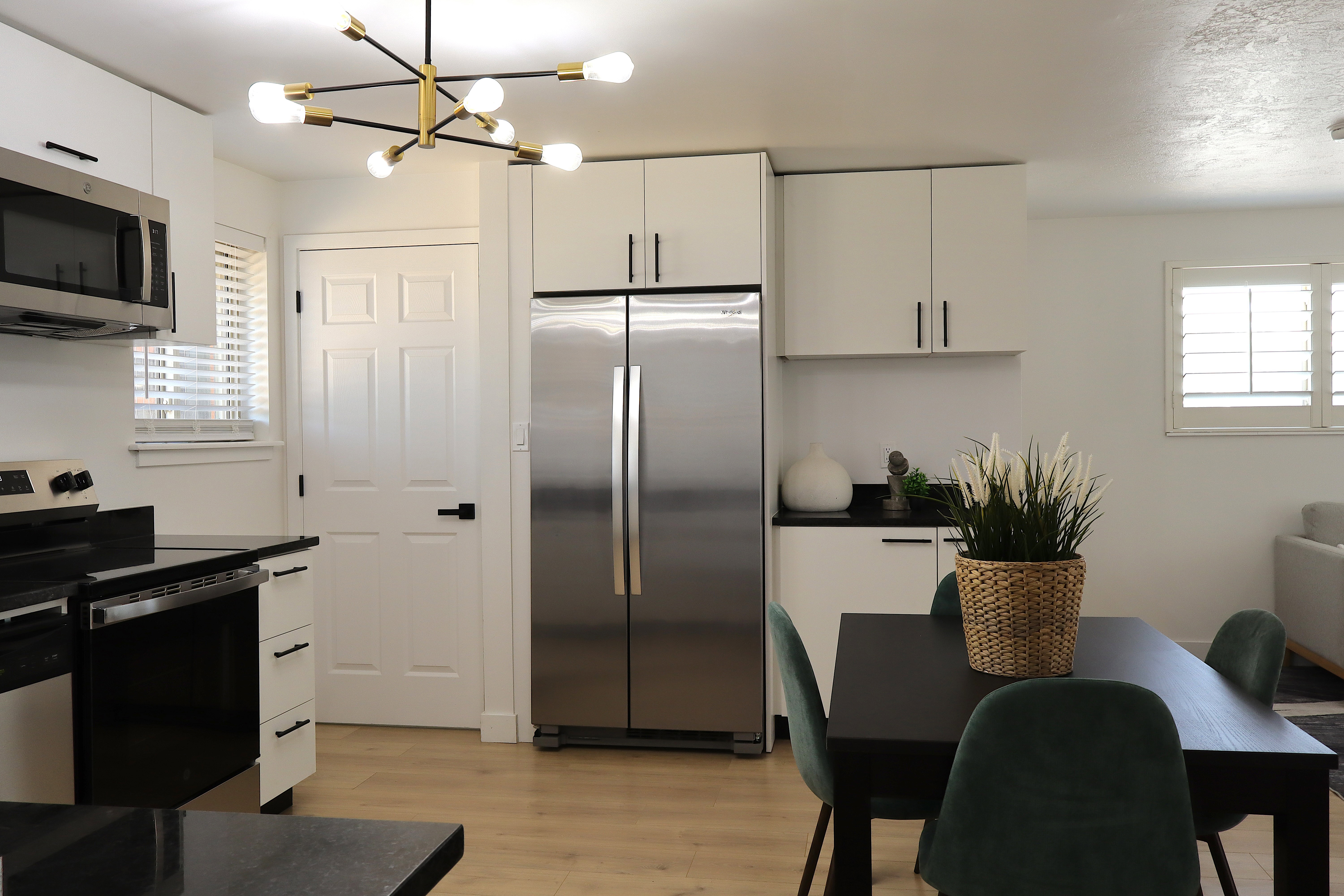 Contemporary kitchen and dining area featuring light wood-finish flooring, white cabinetry with matte black hardware, stainless steel appliances, and dark countertops