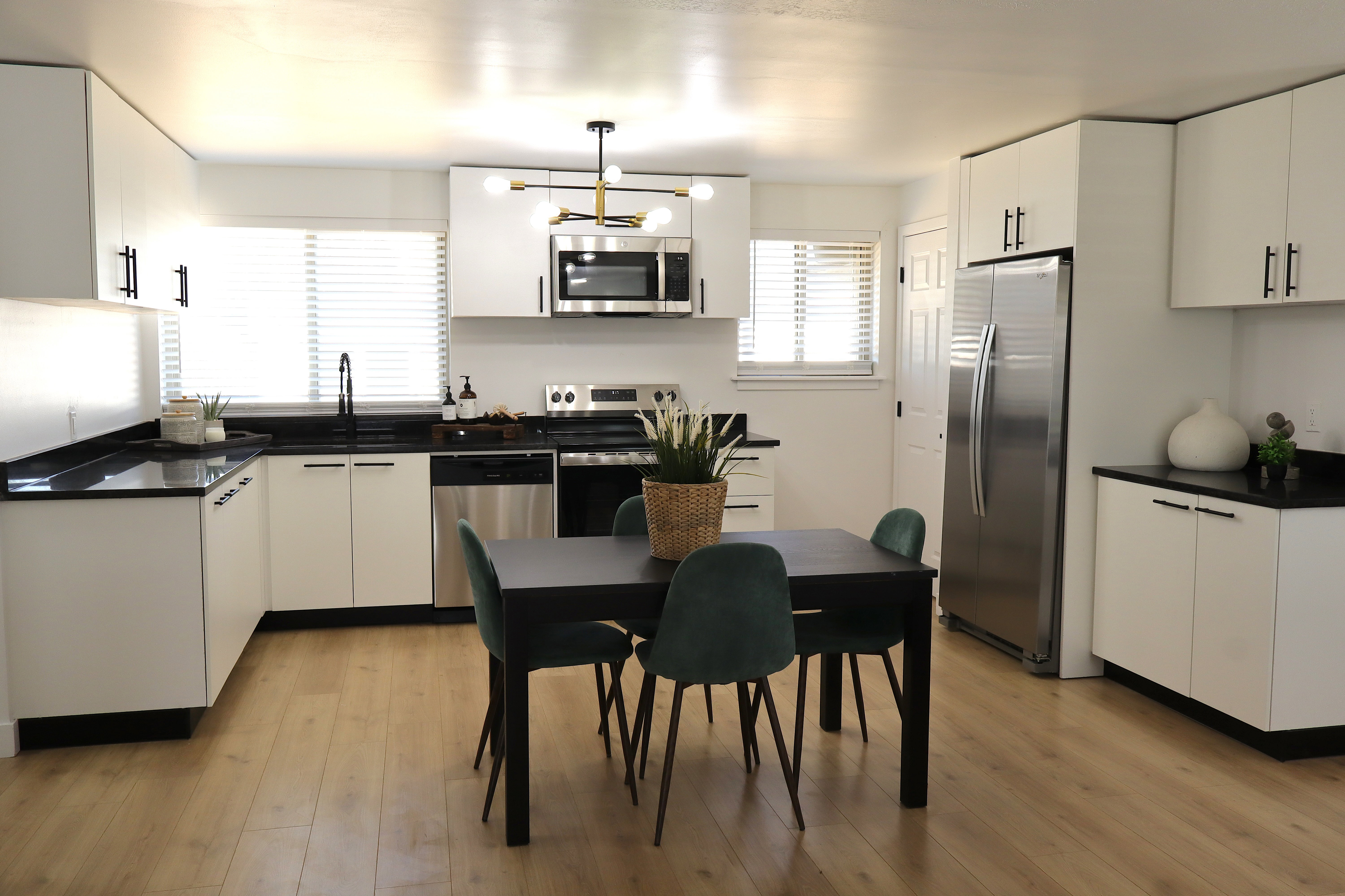 Contemporary kitchen featuring white cabinetry, black countertops, stainless steel appliances, wood-finish flooring, and a modern chandelier