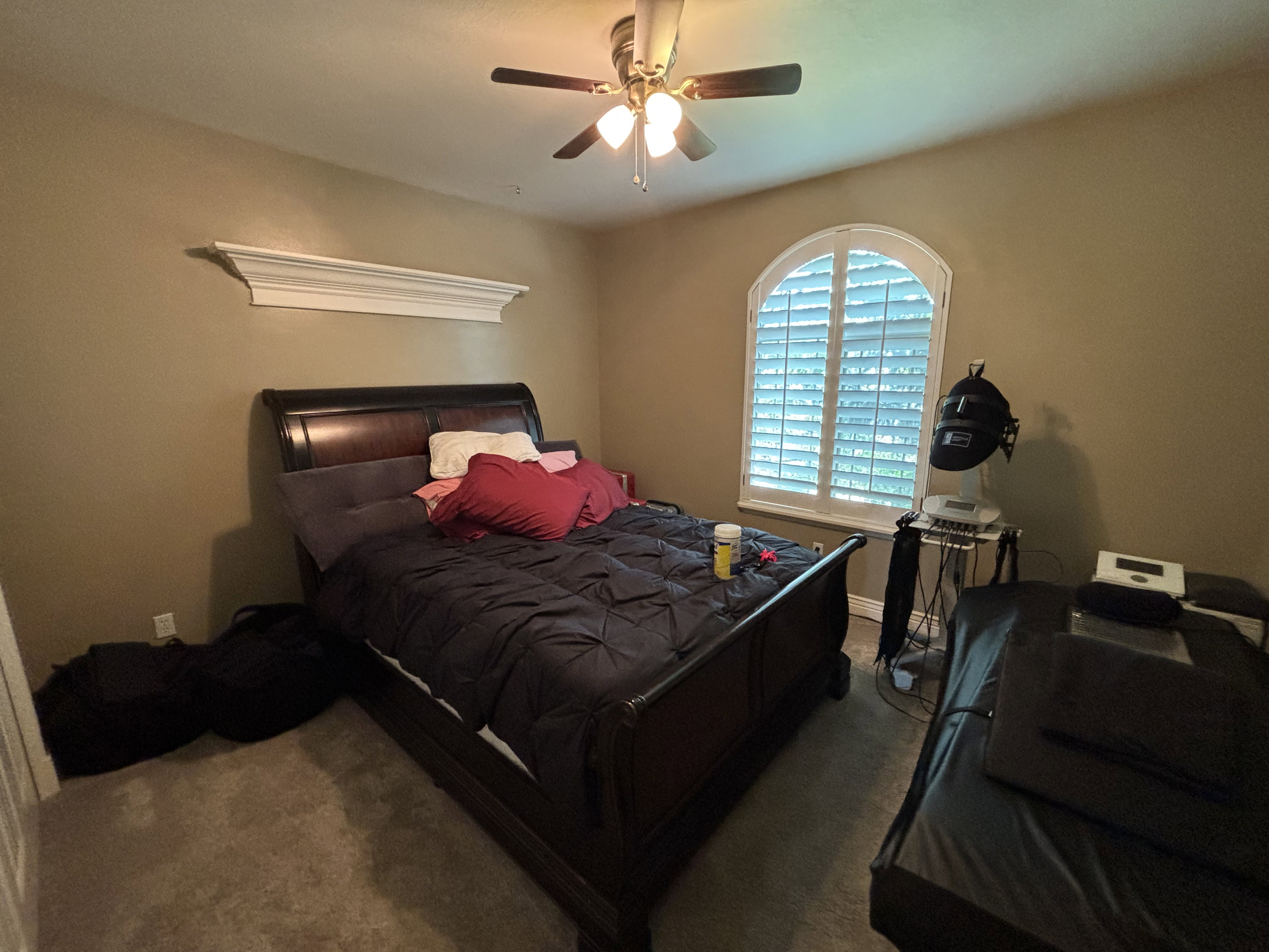 Bedroom featuring an arched window with plantation shutters, a decorative wall shelf, and a ceiling fan with integrated lighting