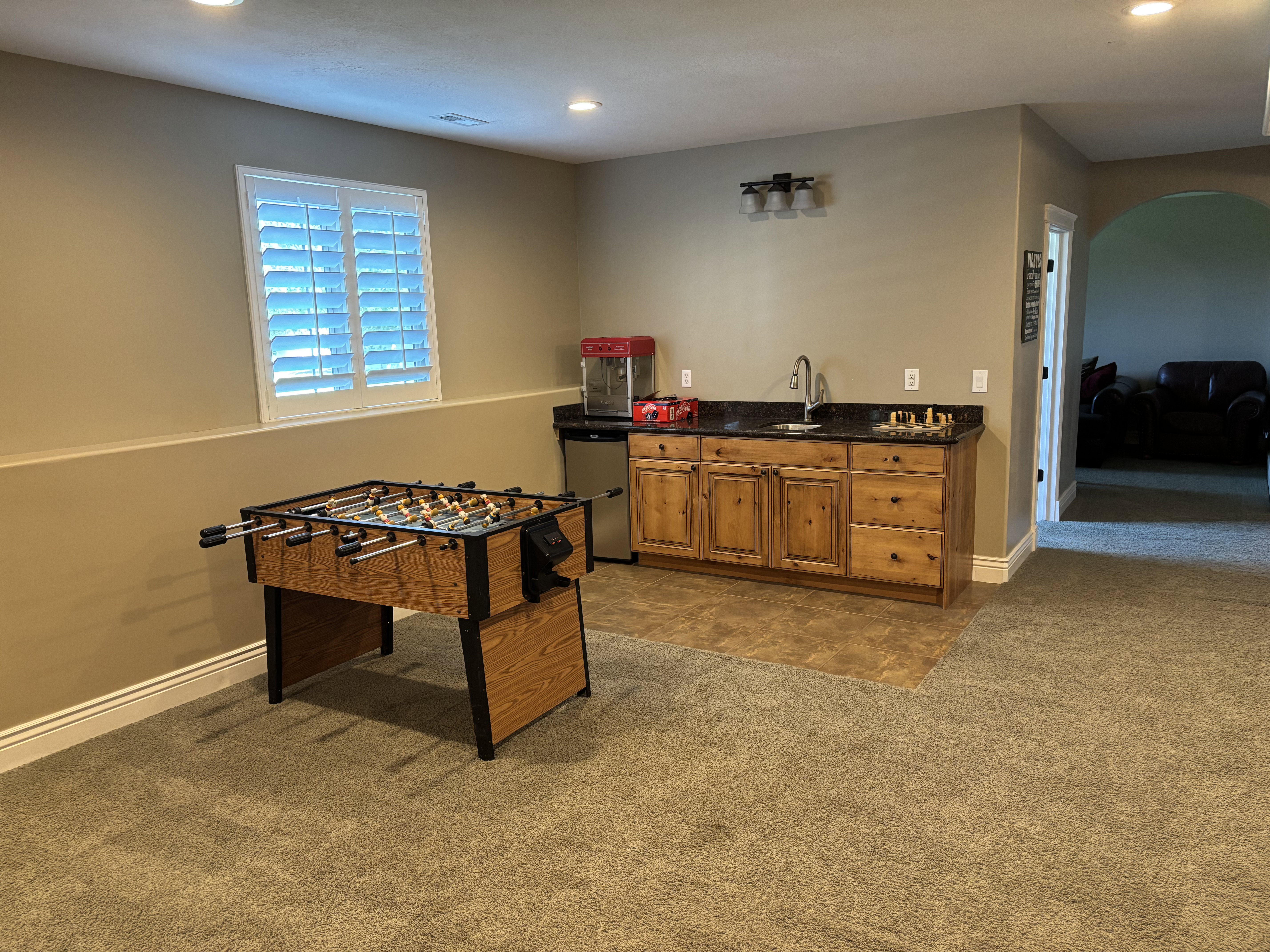 Versatile bonus room featuring recessed lighting, a window with white shutters, and a wet bar with wood cabinetry, a dark countertop, and a stainless steel sink