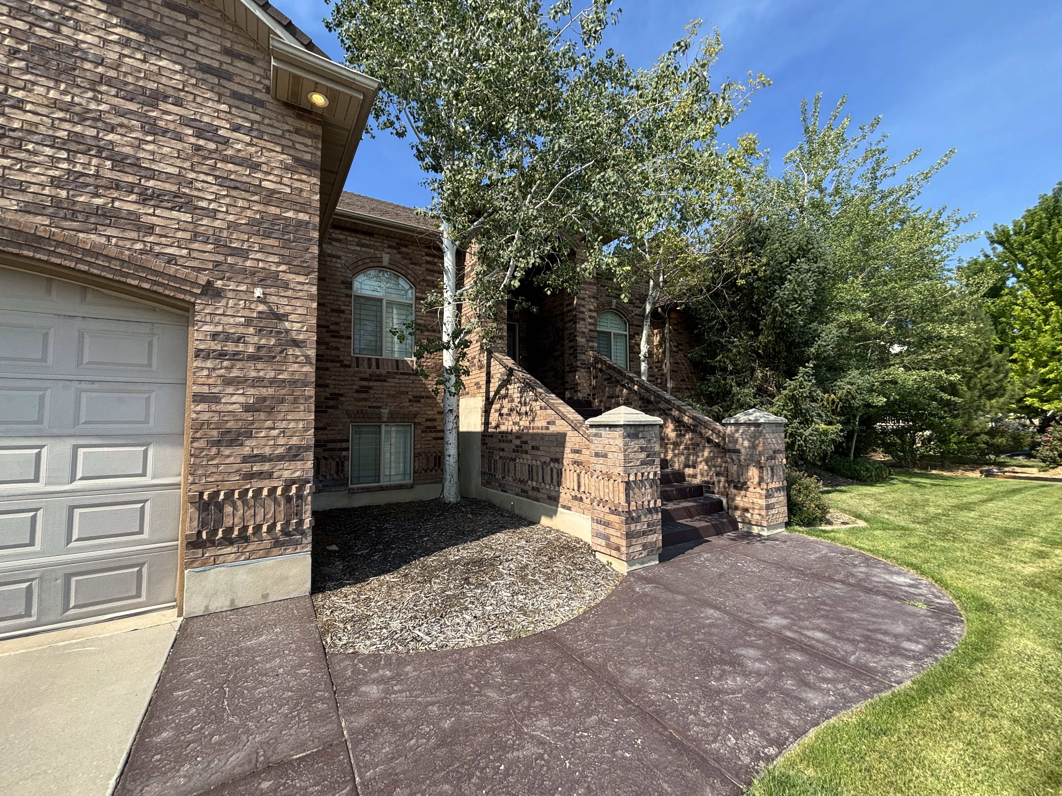 Brick exterior featuring an arched window, a two-car garage with a panel door, and a patterned concrete walkway leading to brick-capped steps