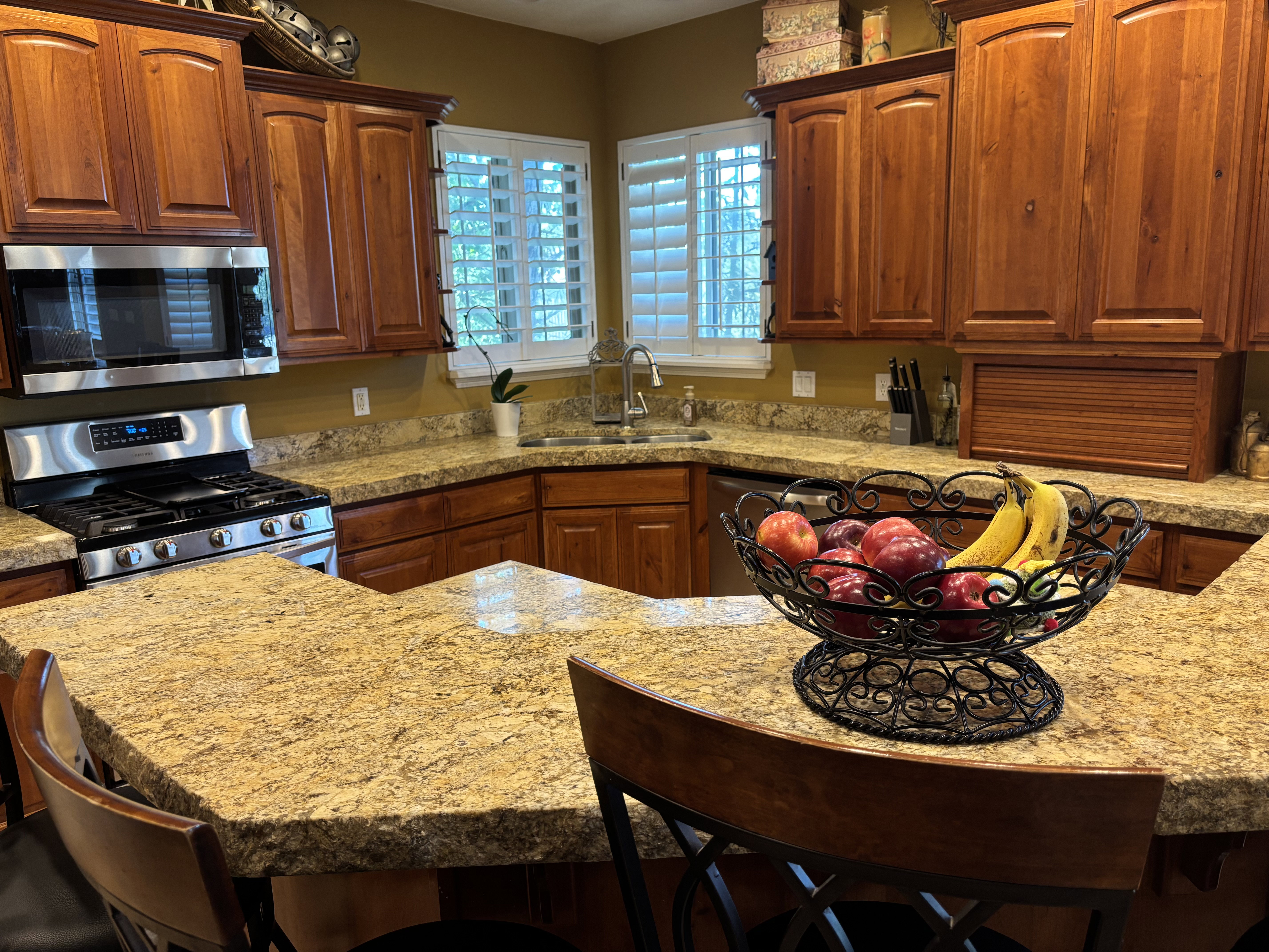 Kitchen featuring an angled breakfast bar, granite countertops, wood cabinetry, stainless steel microwave, and gas range