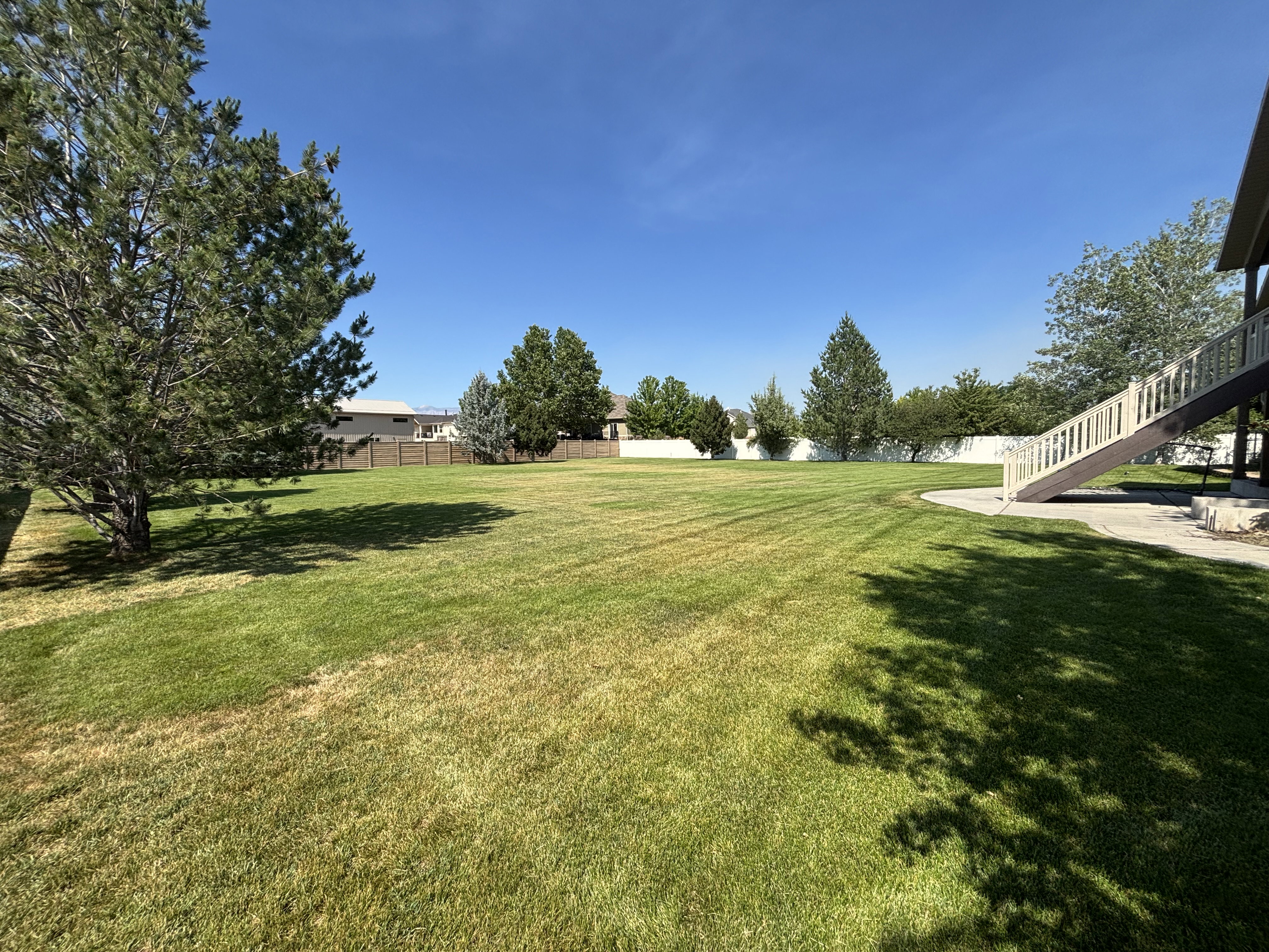 Expansive green lawn with mature trees and a multi-level deck featuring a staircase and white railings