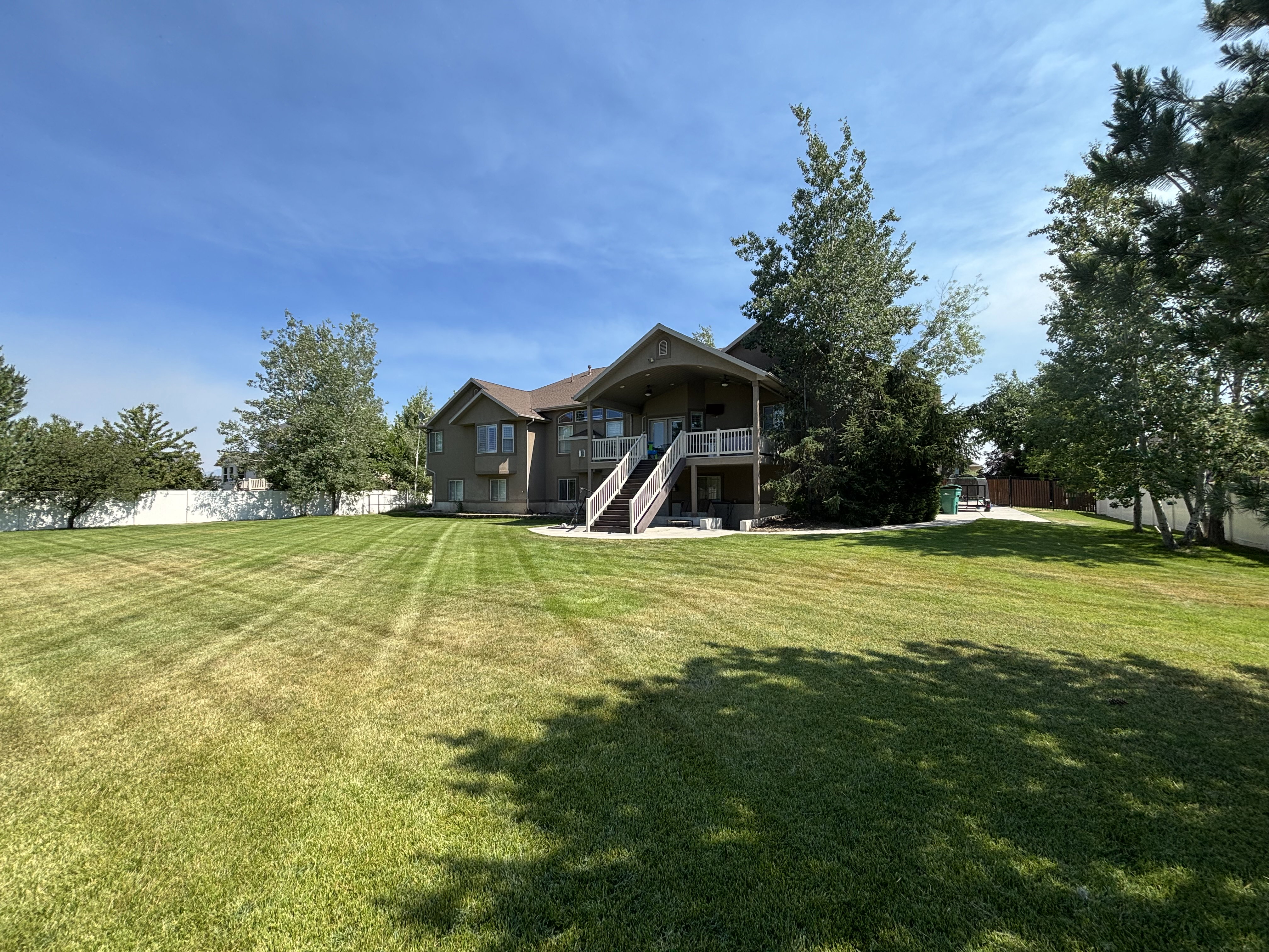 Expansive manicured lawn with mature trees and a privacy fence