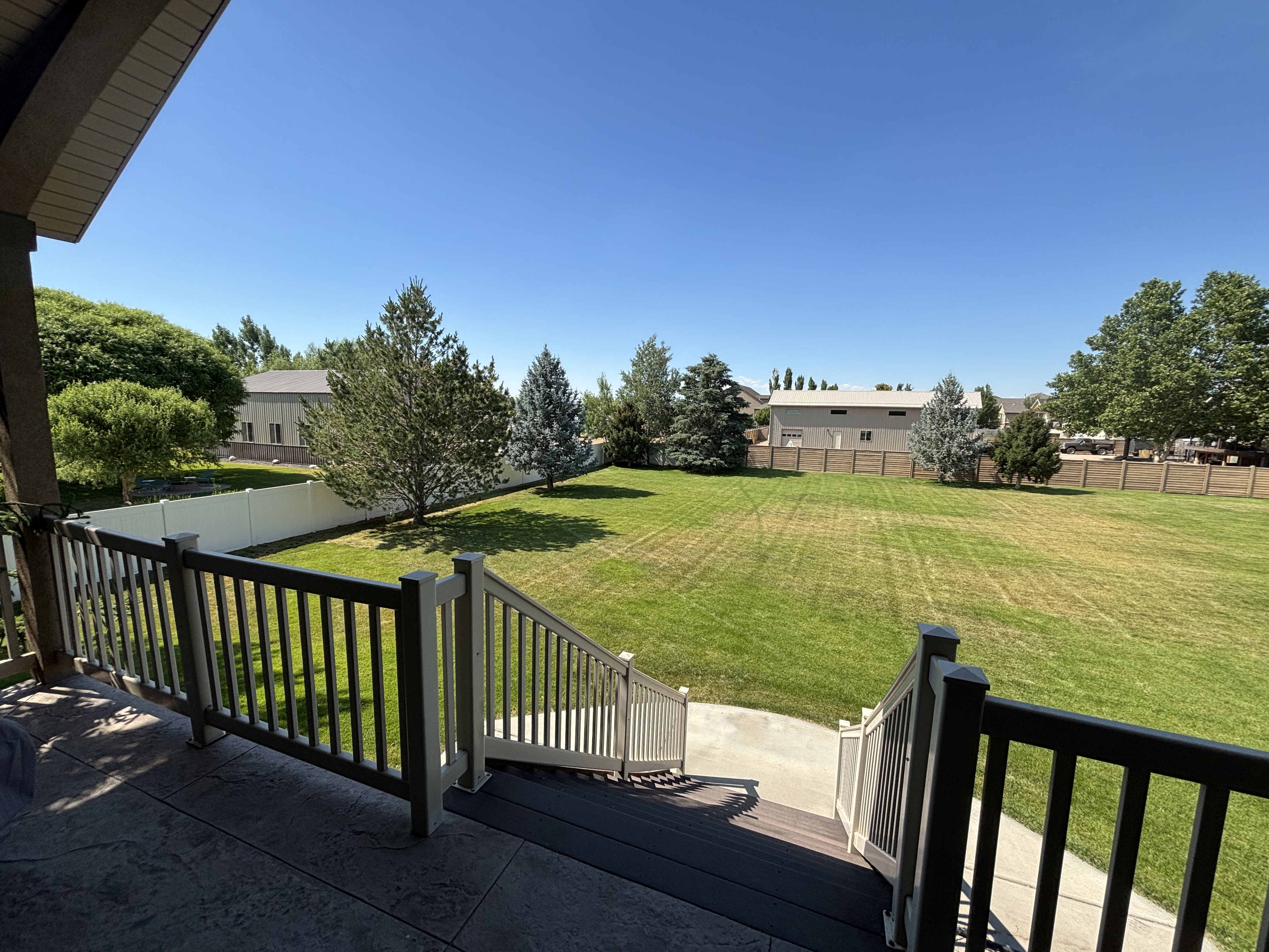 Expansive green lawn framed by a white privacy fence and mature trees