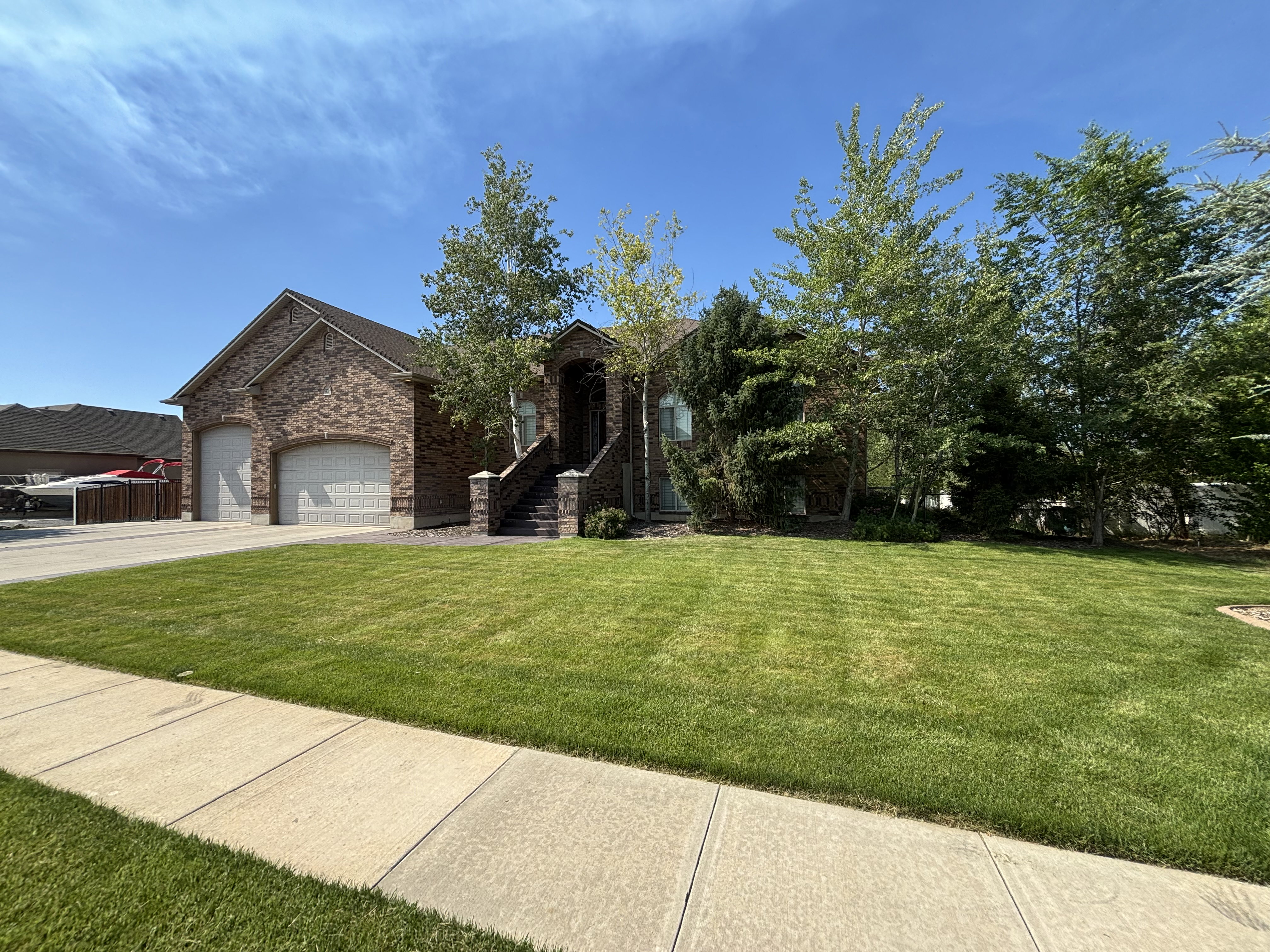Brick exterior home featuring a two-car garage with arched doors, a dedicated front entry staircase, and a generously sized front lawn
