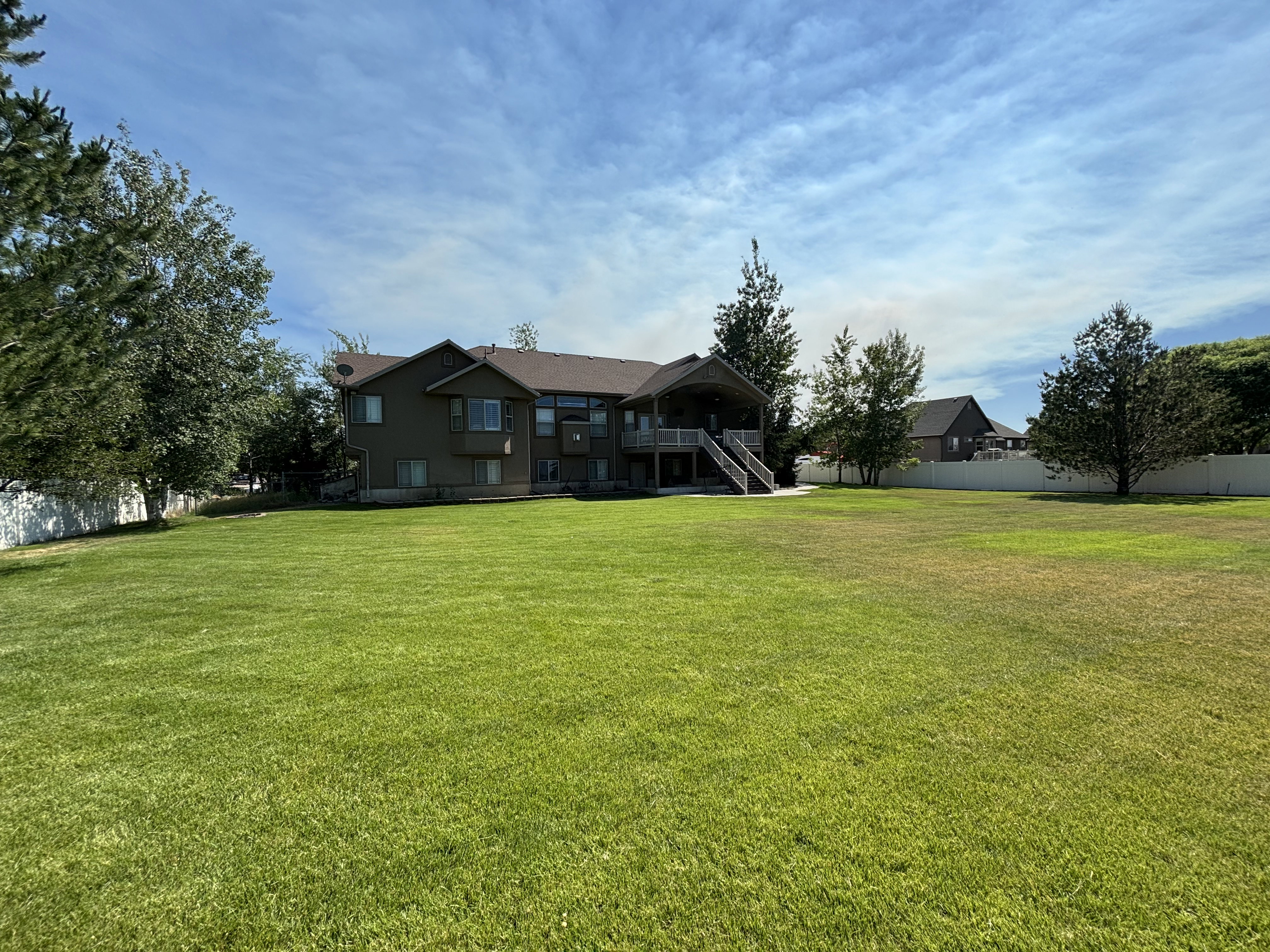 Expansive green lawn with mature trees and a vinyl privacy fence