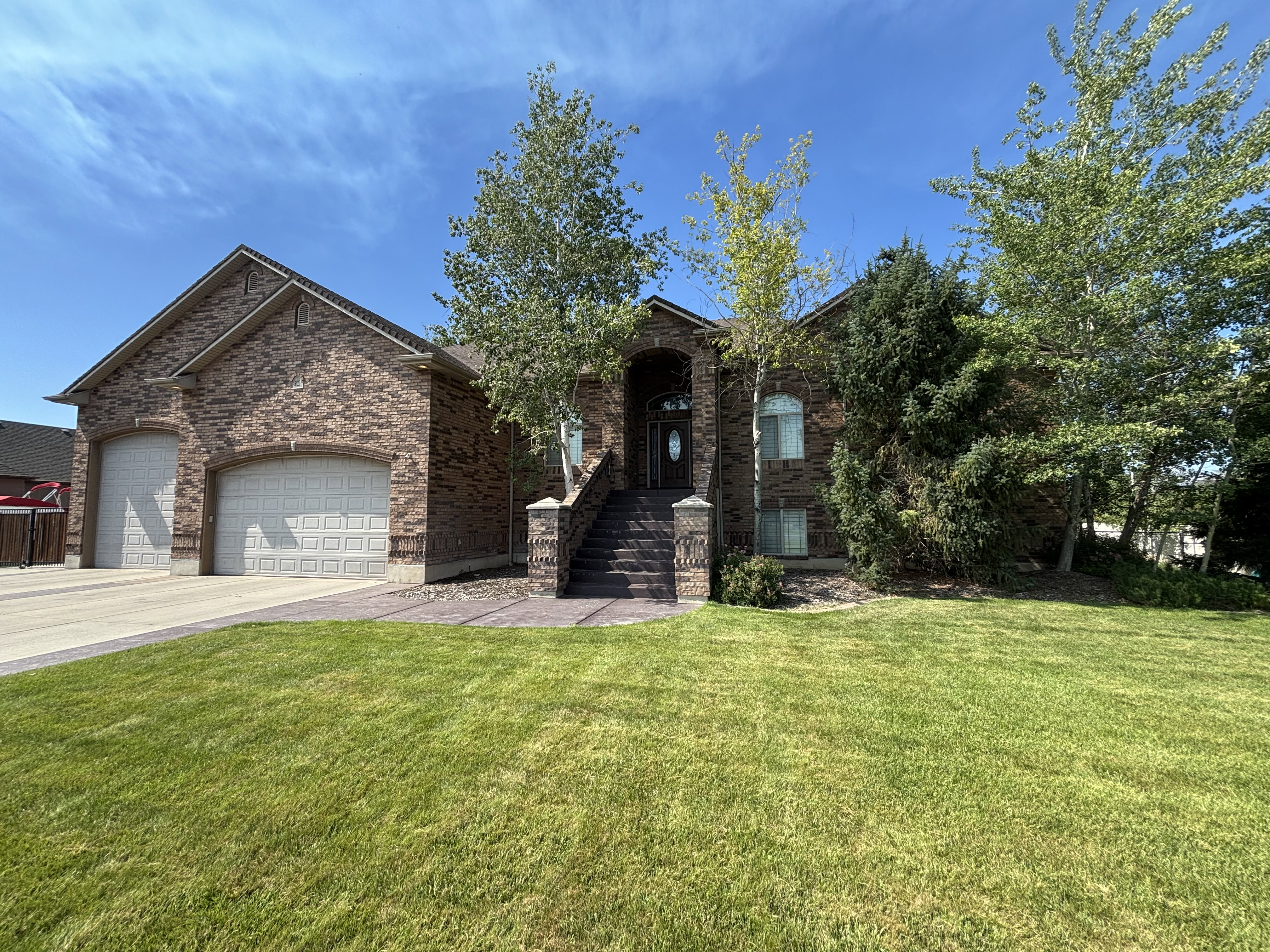 Brick exterior featuring a prominent two-car garage with arched entrances, a grand entry staircase, mature trees, and a manicured lawn