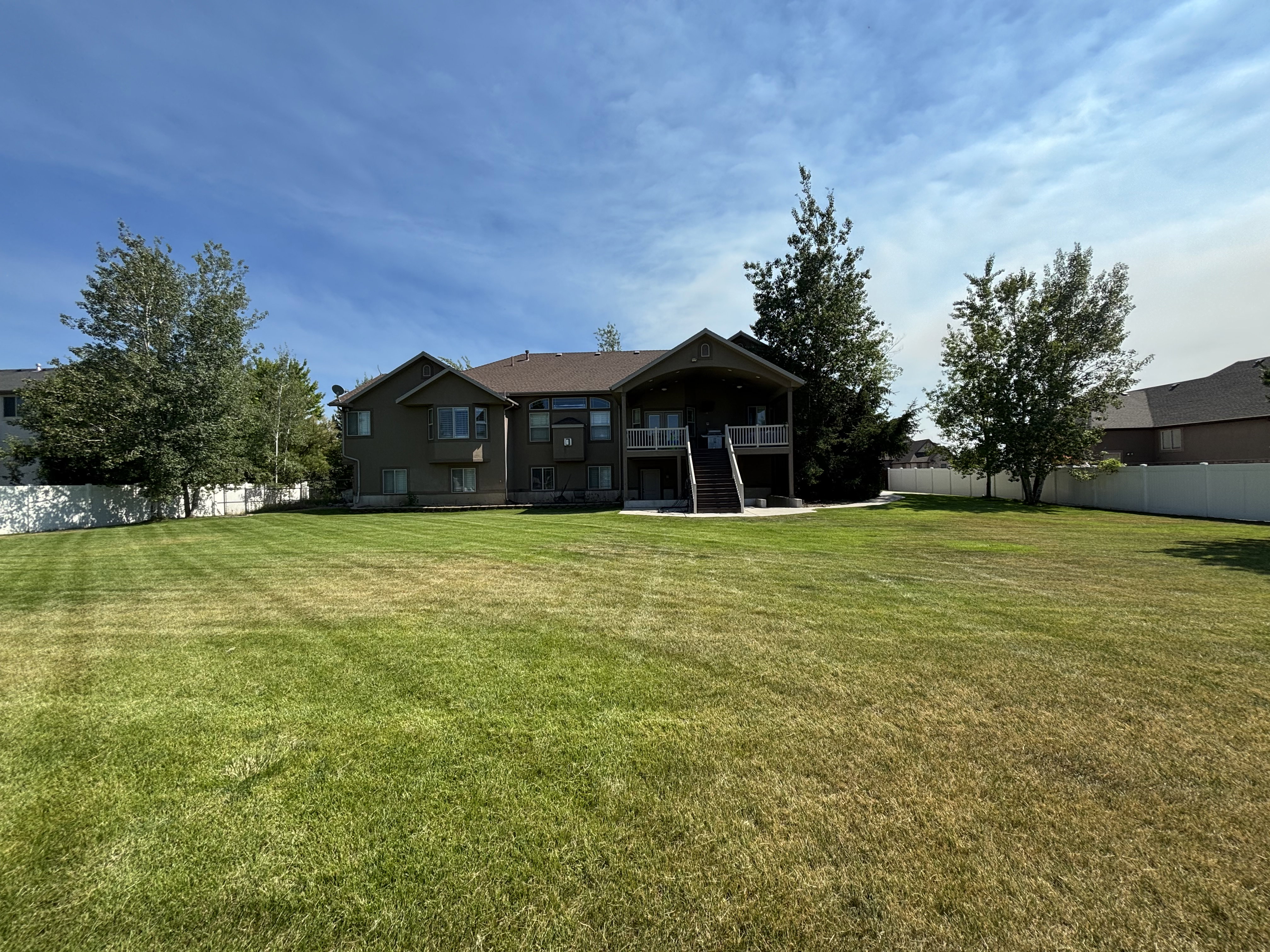 Expansive backyard featuring a manicured lawn, mature trees, and a full privacy fence