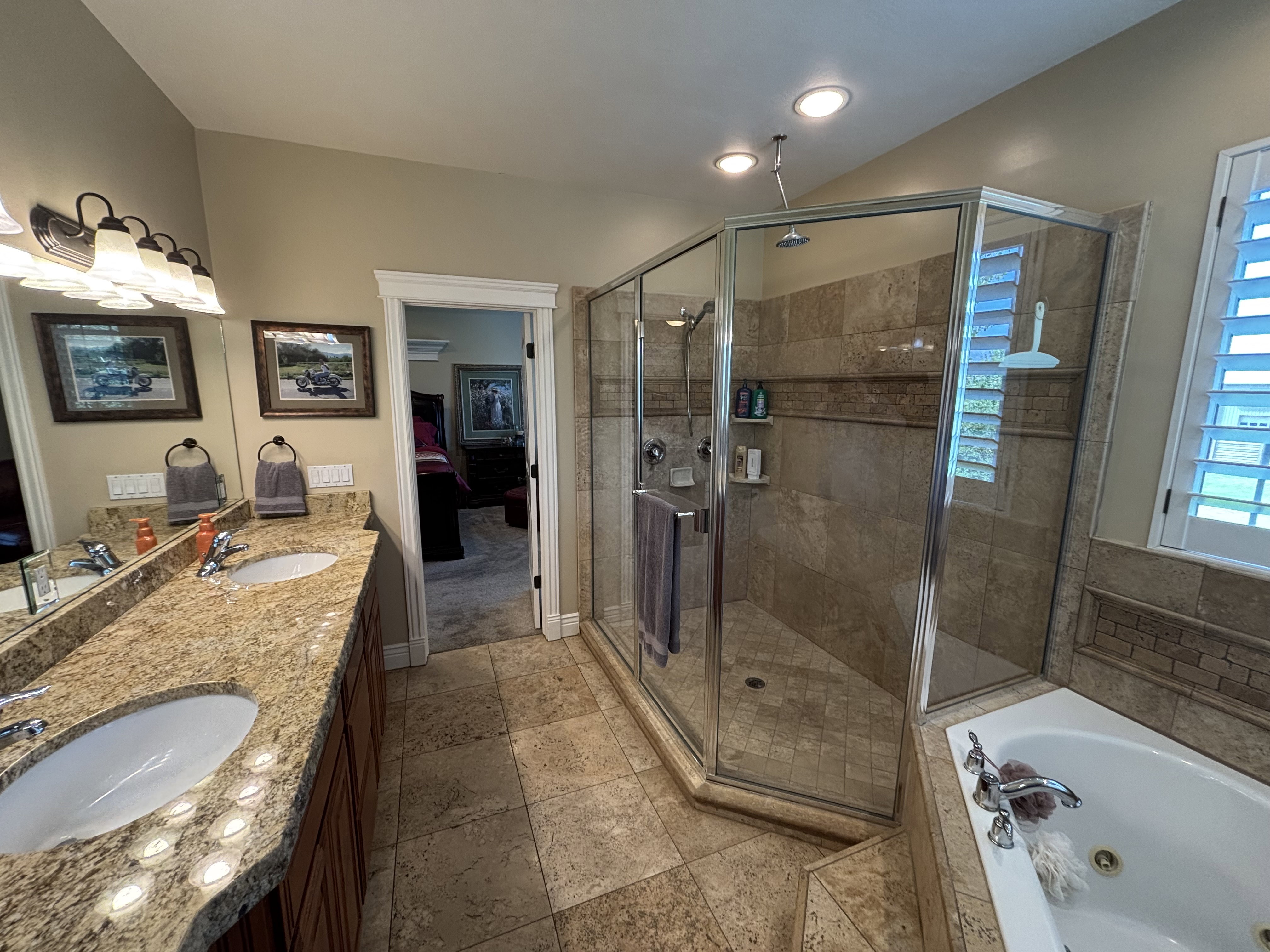 Bathroom featuring a dual vanity with a granite-finish countertop, undermount sinks, a glass-enclosed shower with tiled walls, a separate built-in soaking tub, and tile flooring