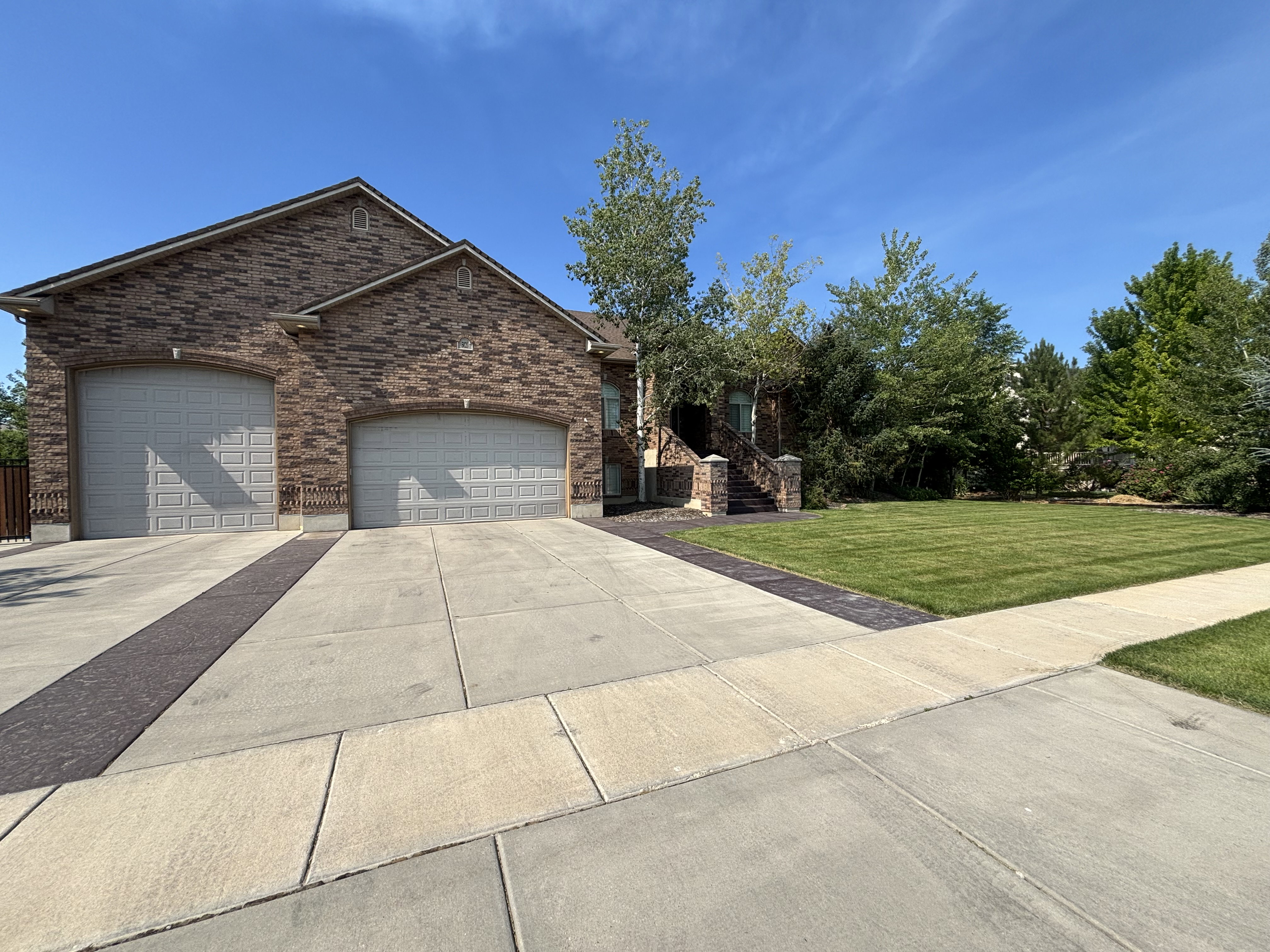 Brick facade home featuring a two-car garage, patterned concrete driveway, and expansive front lawn