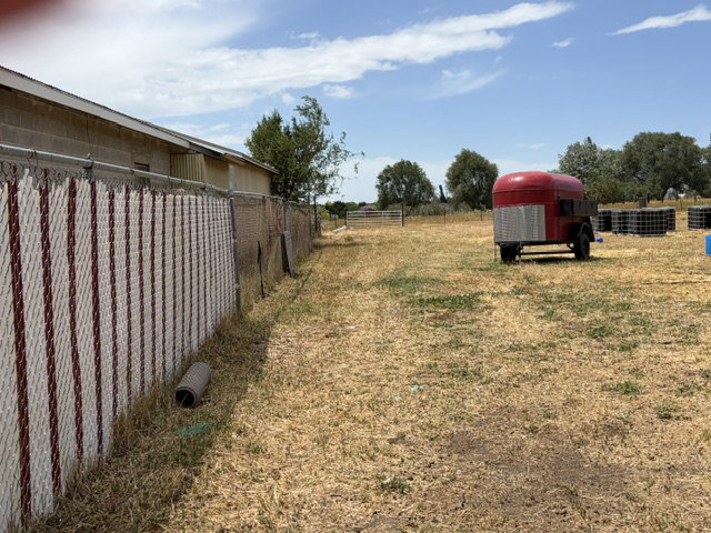 Expansive parcel featuring a chain-link fence with privacy slats, open field space, and distant mature trees