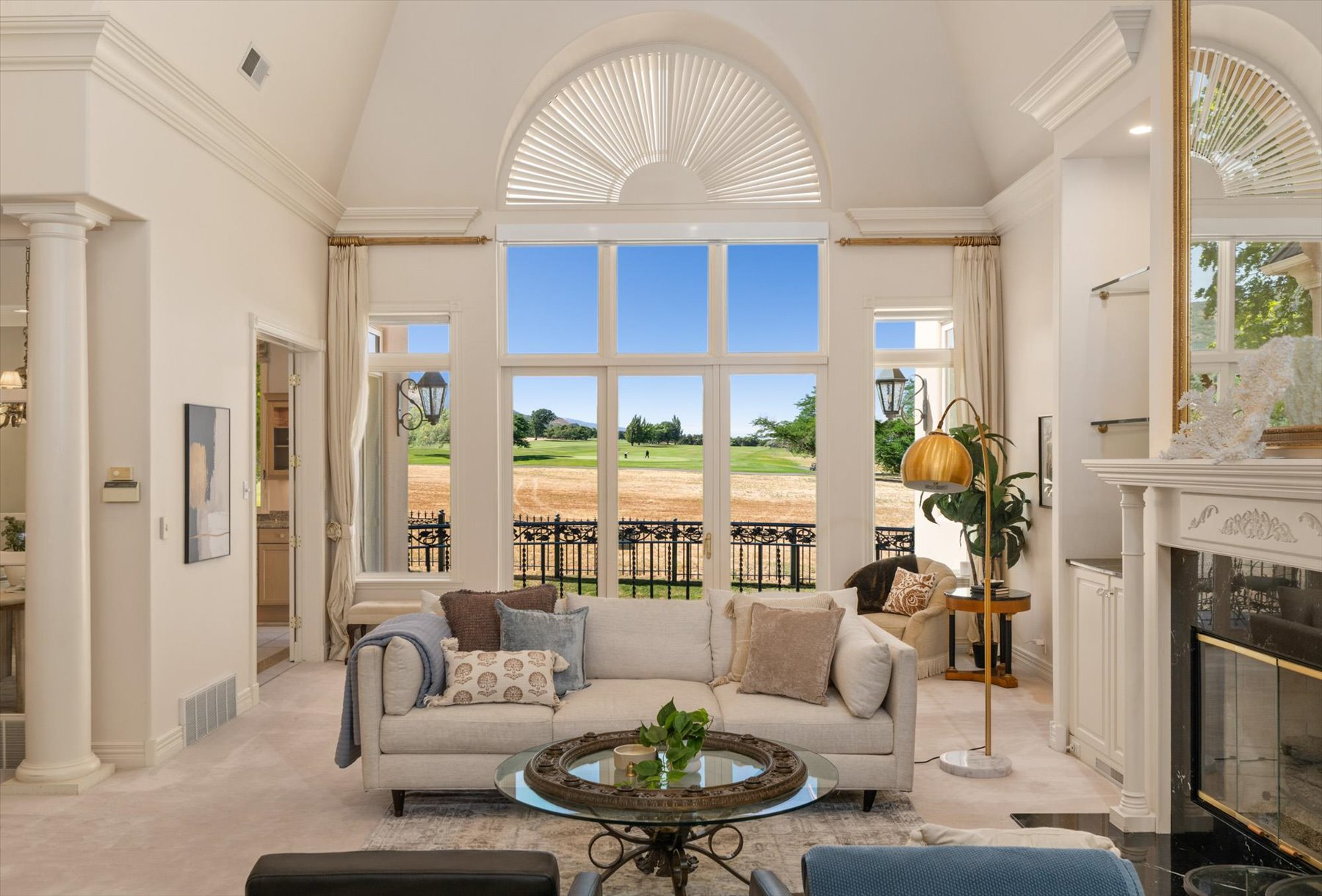 Grand living space featuring a soaring vaulted ceiling with crown molding, an arched transom window, and a full-height glass window wall overlooking expansive natural surroundings