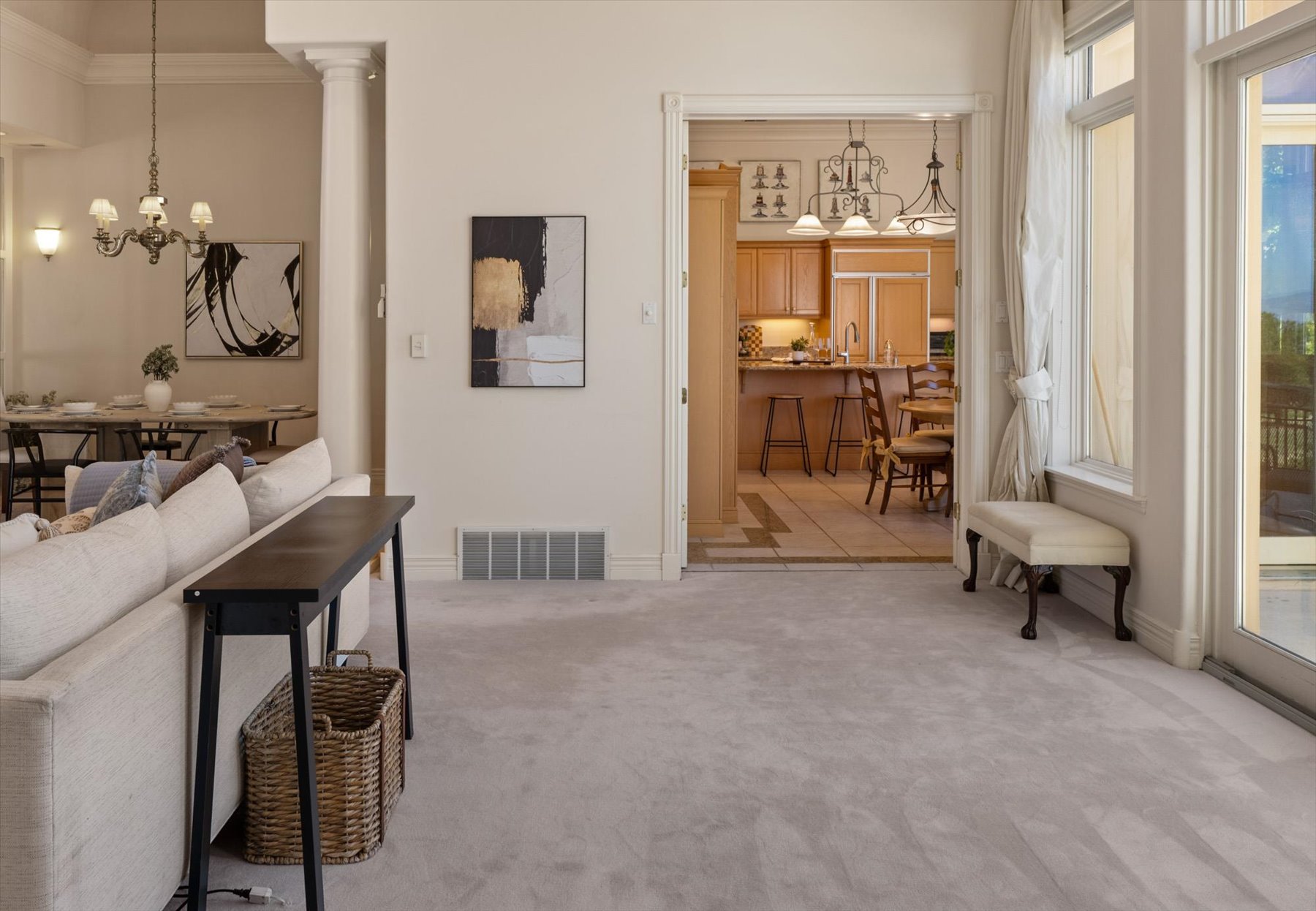 Carpeted living area with a wide entryway to the kitchen featuring wood cabinetry and tile flooring