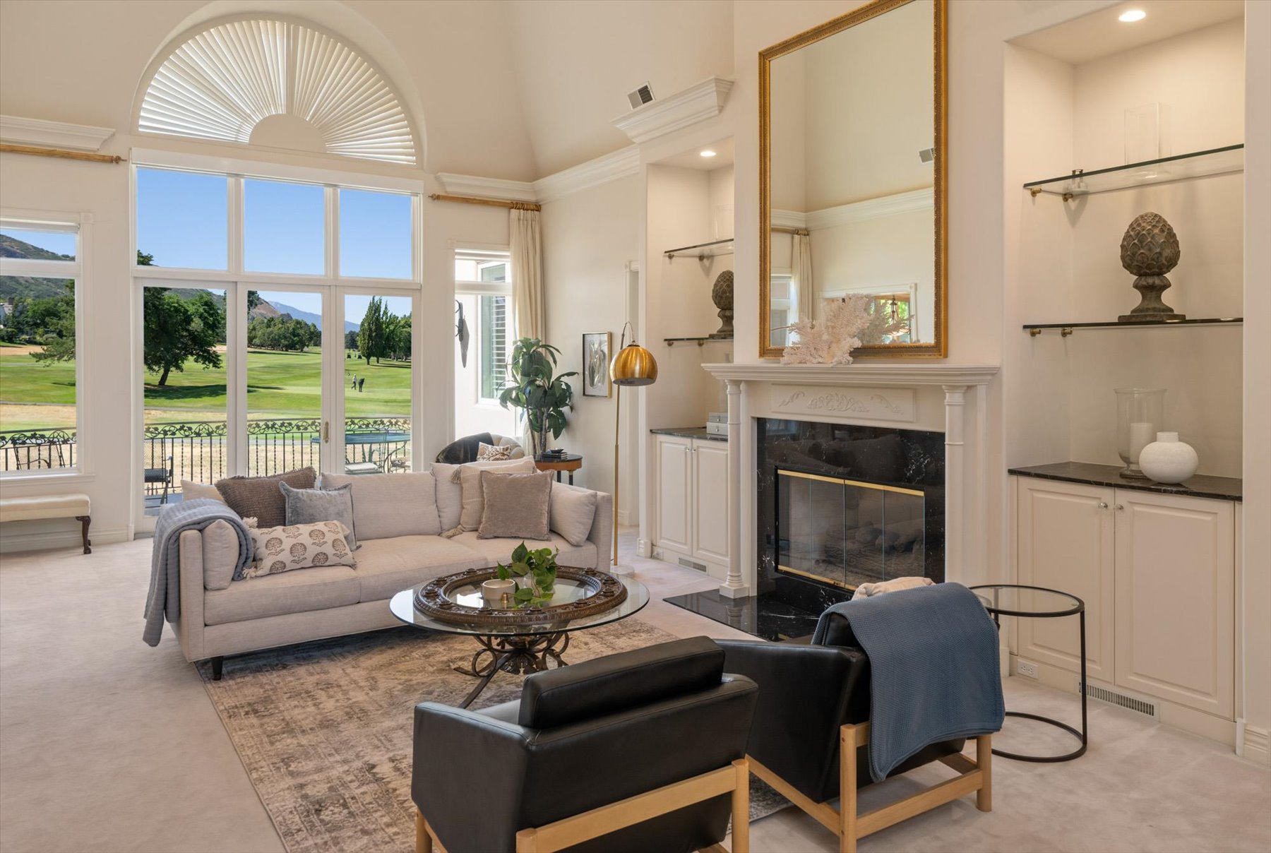 Vaulted ceiling living area featuring a prominent arched window, fireplace, built-in cabinetry with dark countertops, and integrated glass shelving