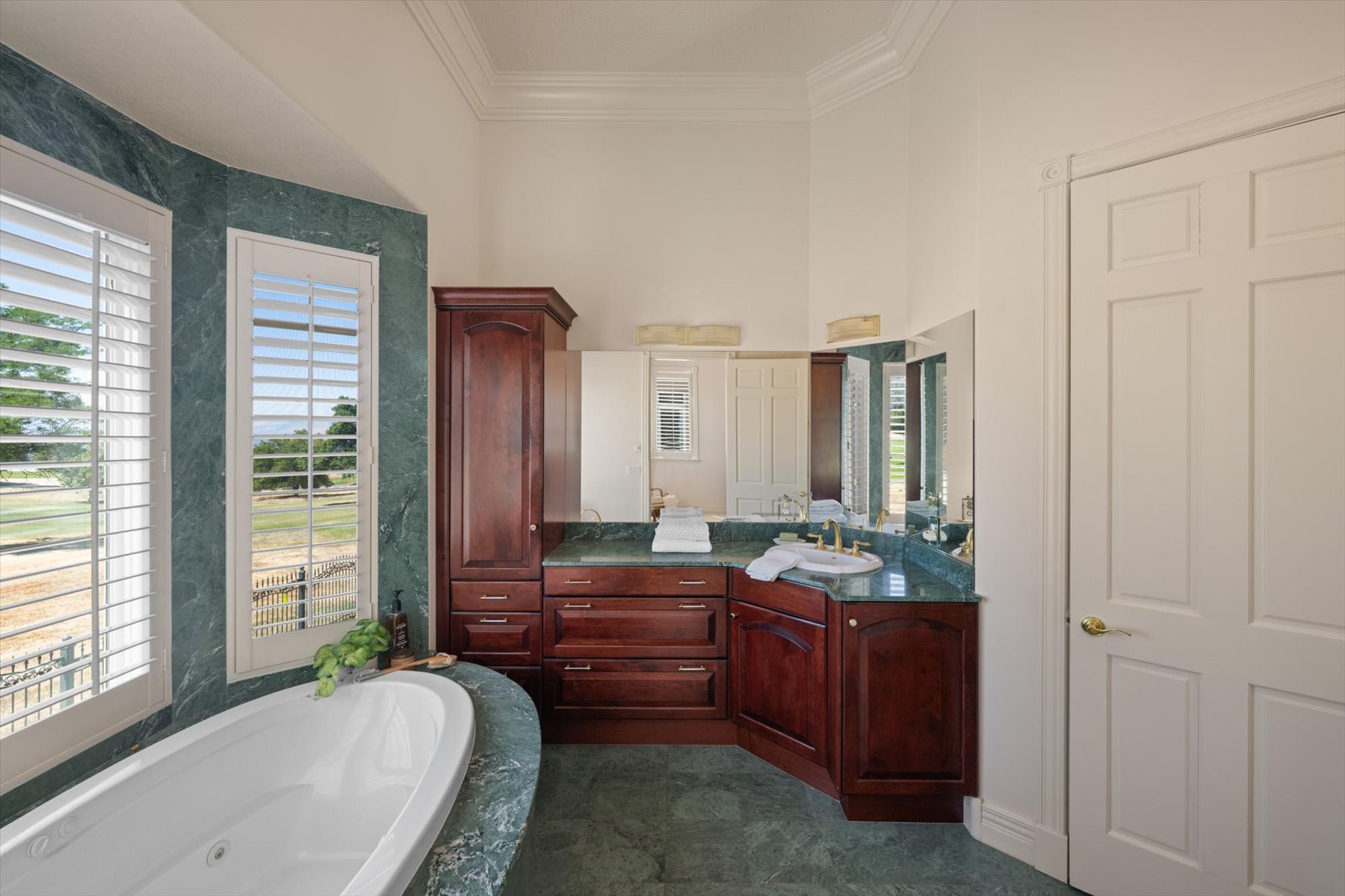 Bathroom featuring a freestanding soaking tub, expansive vanity with integrated sink, richly stained cabinetry, and large windows with plantation shutters