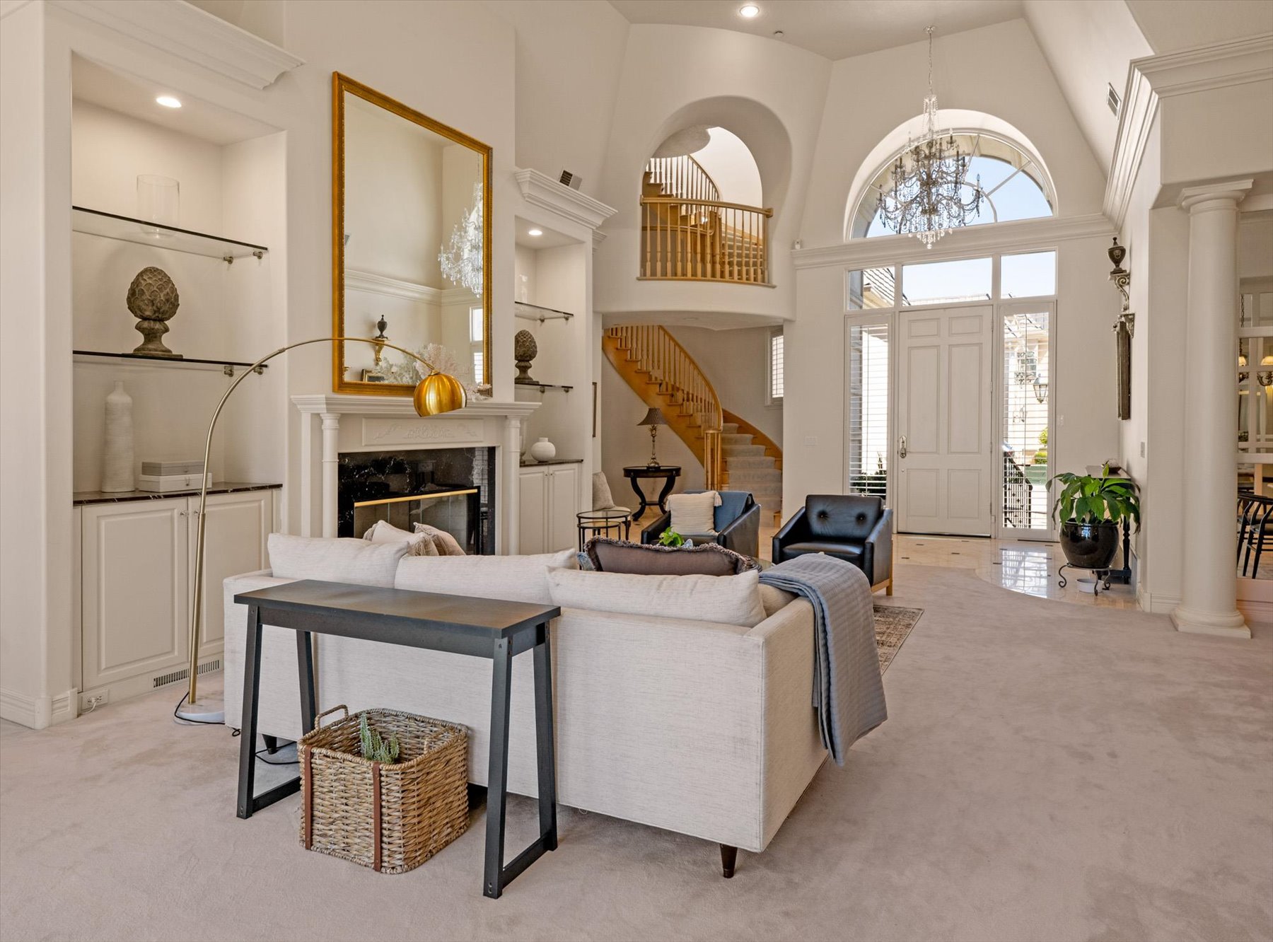 Spacious living area featuring a fireplace with a white mantel, built-in shelving with glass inserts, and high ceilings